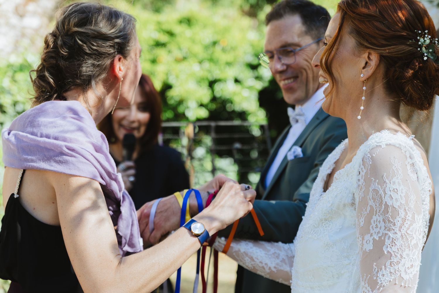 A handfasting wedding ceremony with colorful ribbons being tied around the couple's hands by an officiant outdoors.