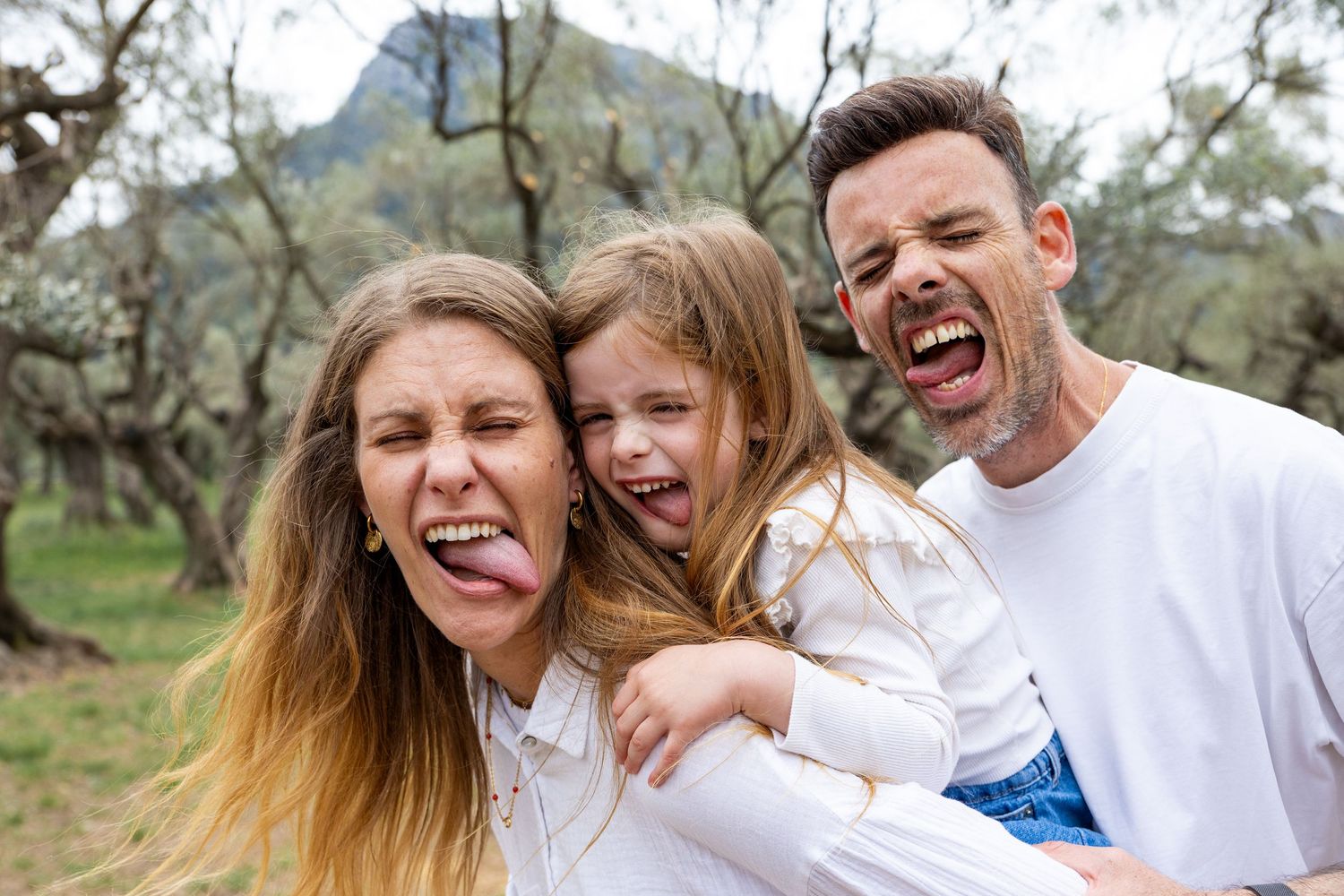 A playful family of three sticks out their tongues together in a fun outdoor portrait.