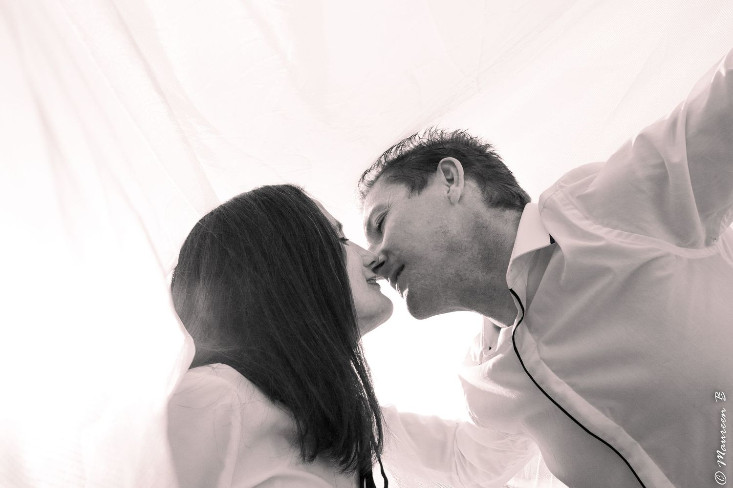 Black and white romantic photo of a couple sharing a tender kiss in soft light.