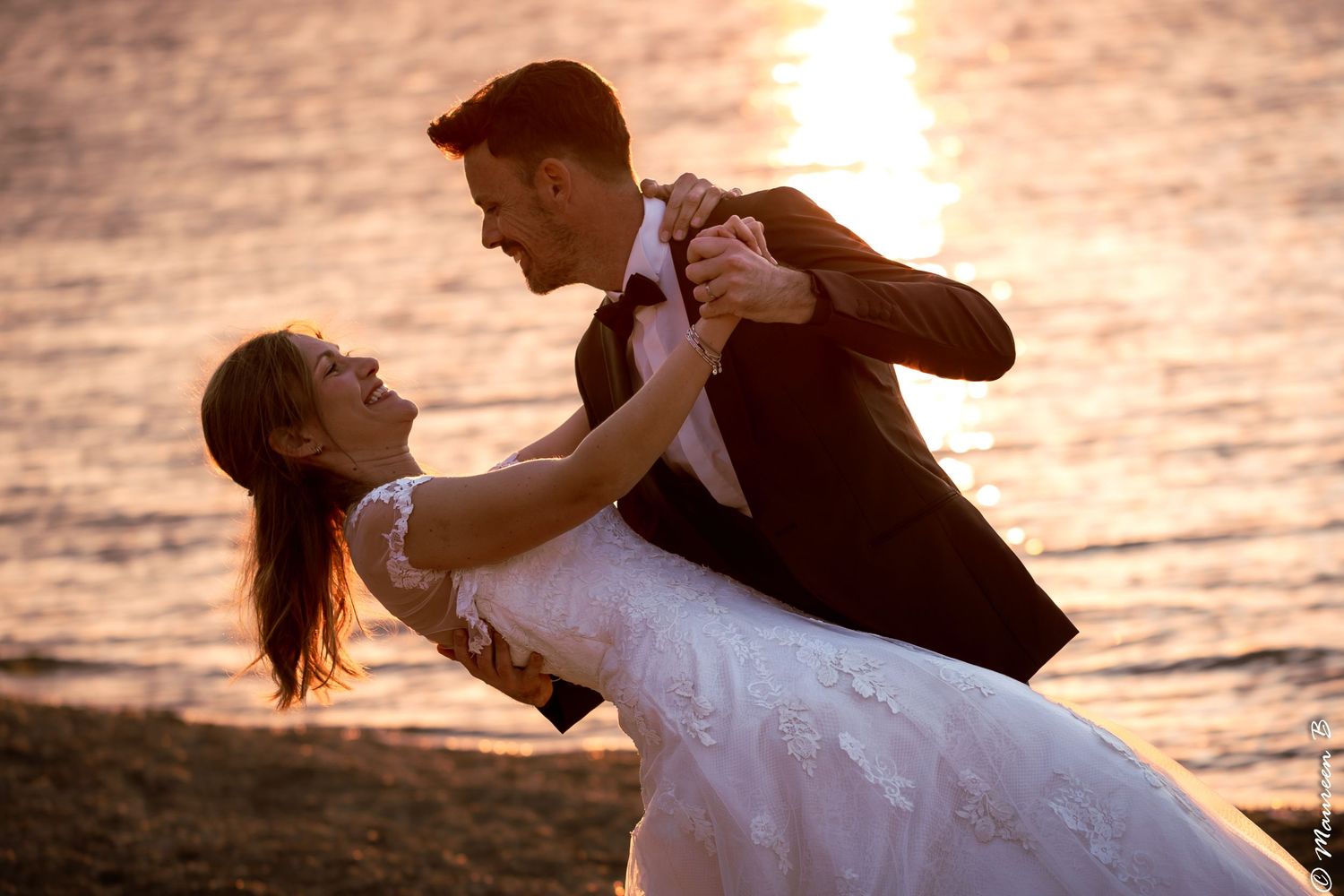 Bride and groom sharing romantic dance on beach during golden sunset.