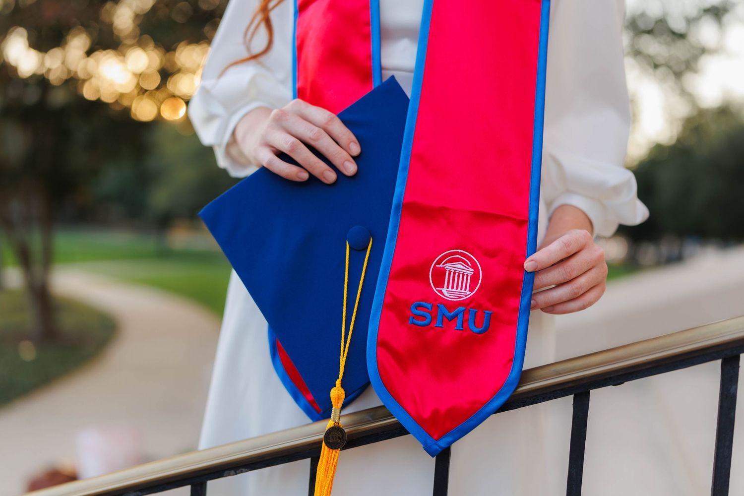 Close-up of hands holding blue graduation cap and red SMU honor stole.