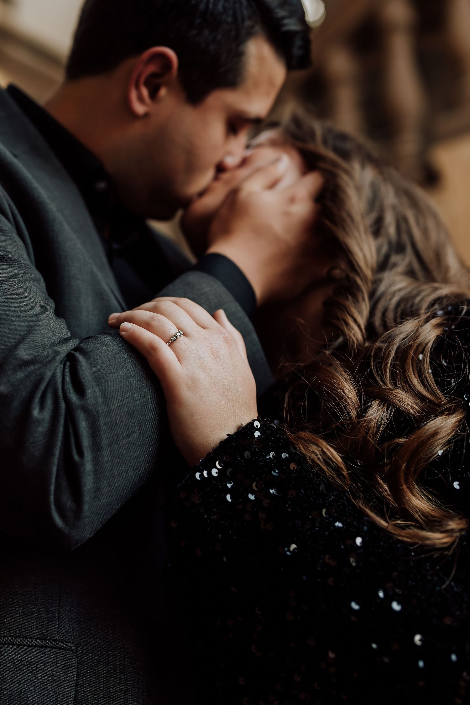 Close-up of couple kissing with focus on engagement ring and curly hair detail.