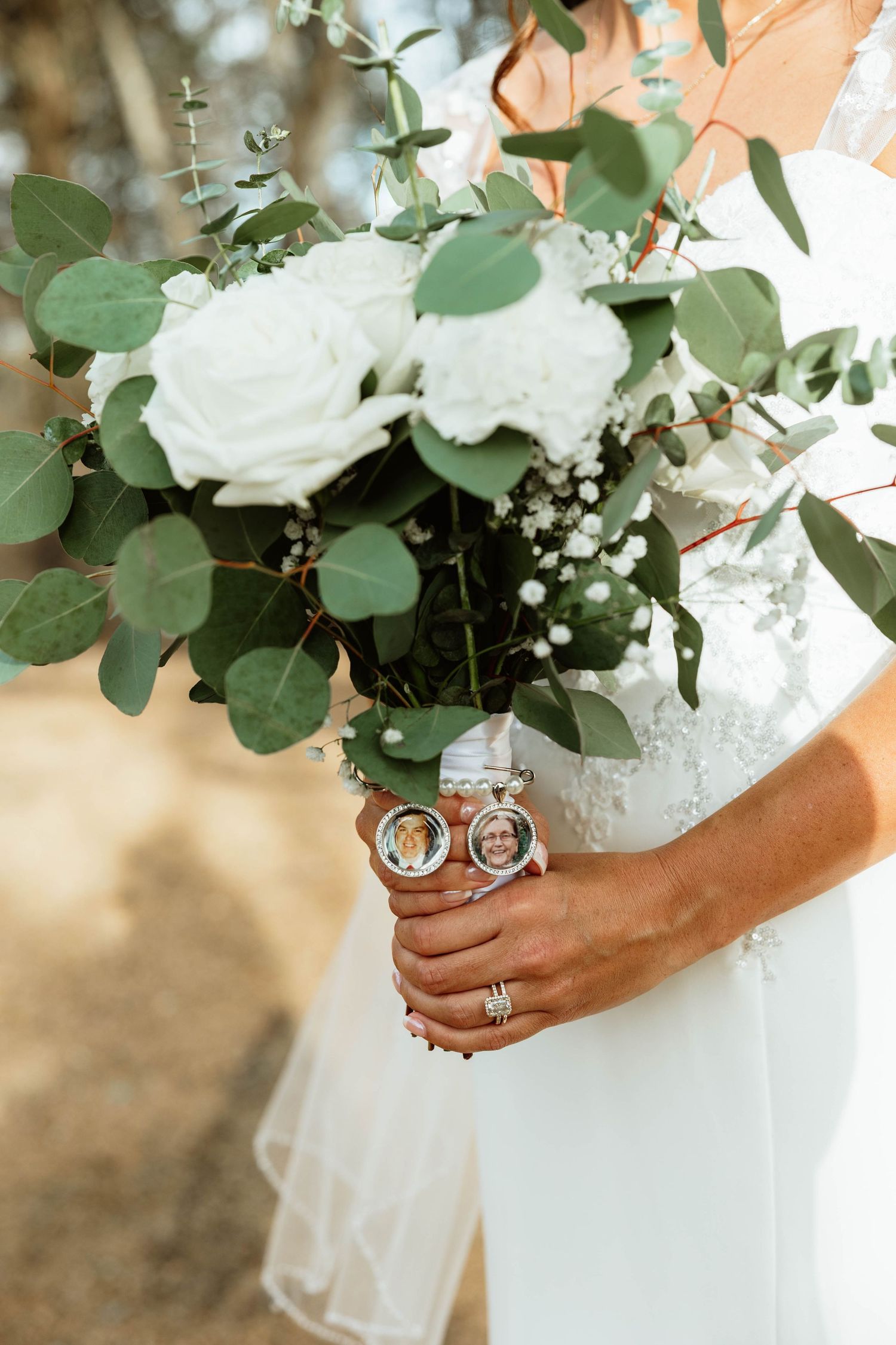 Close-up of bridal bouquet with white roses and eucalyptus featuring memorial photo charms.
