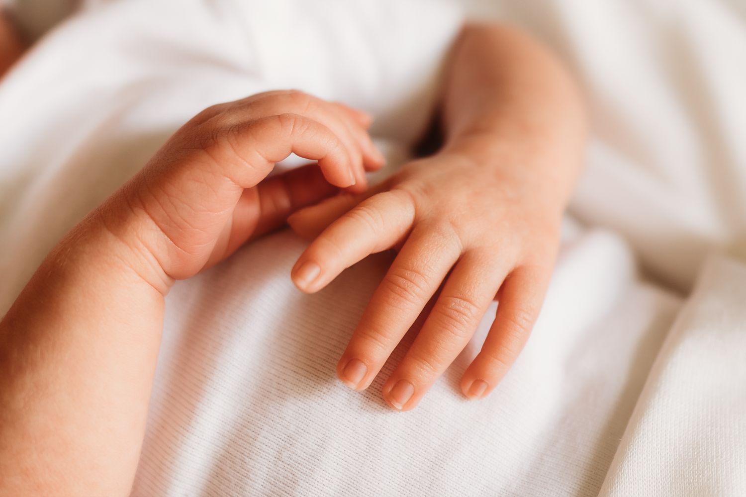 Close-up of an adult hand gently holding a newborn baby's tiny hand on a white blanket.