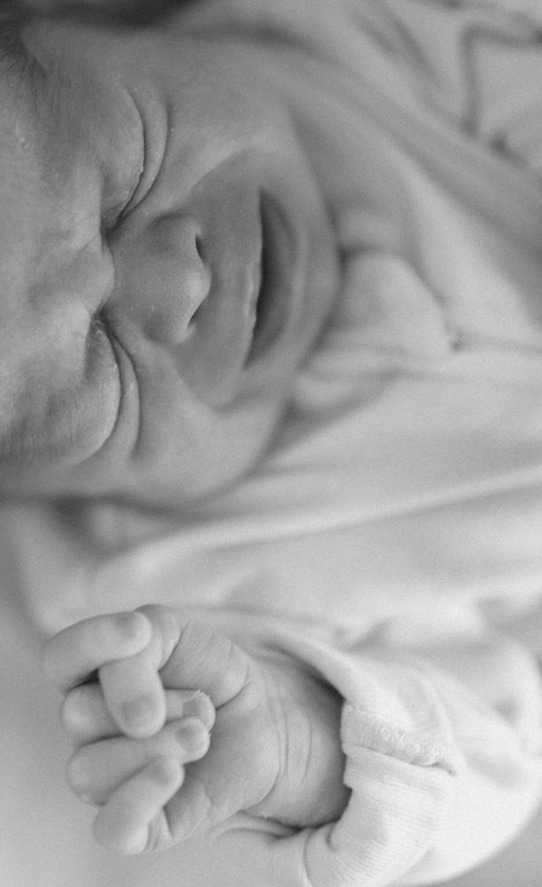 Black and white close-up of sleeping newborn baby face and tiny clenched fist.