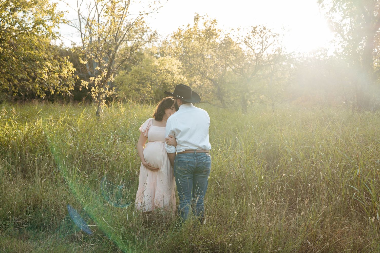 Couple walking through sunlit meadow during outdoor maternity photo session.