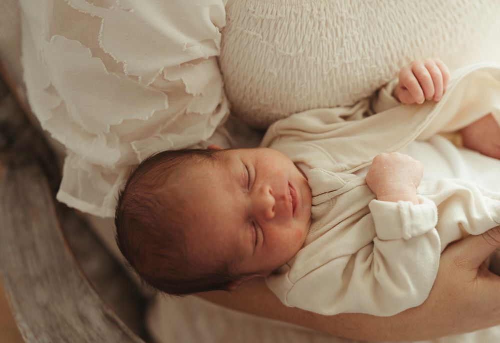 Sleeping newborn baby cradled in mother's arms wearing a cream onesie.
