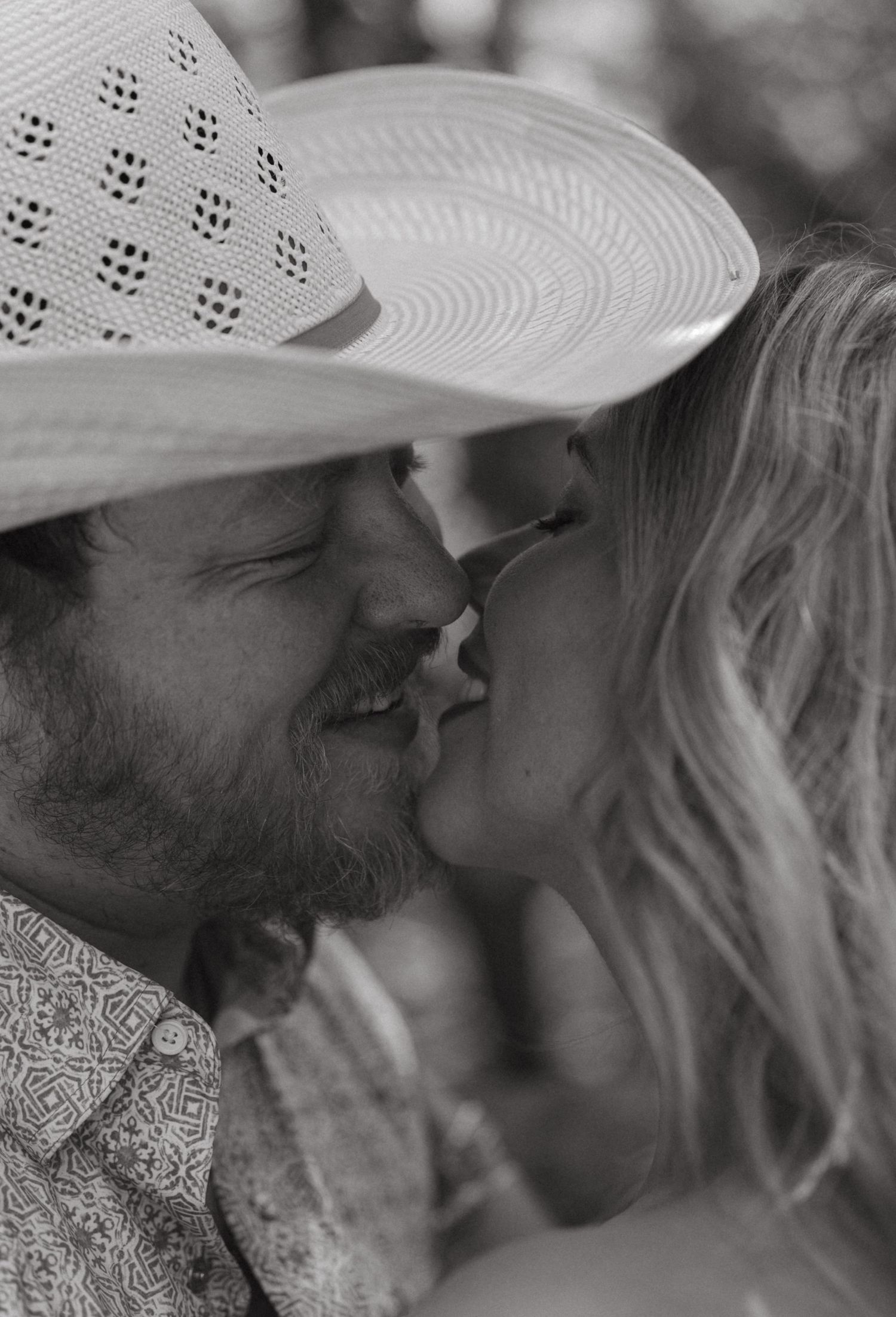 Black and white close-up of a couple sharing a romantic kiss, man wearing a straw cowboy hat.