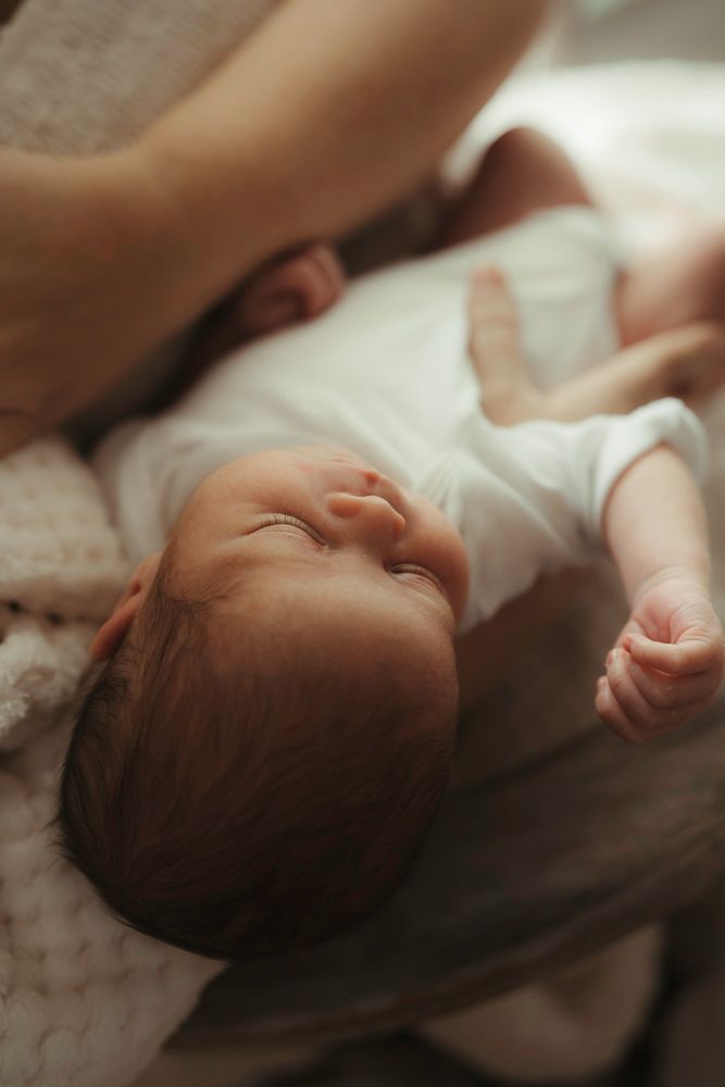 Newborn baby in white onesie sleeping peacefully on a soft blanket.