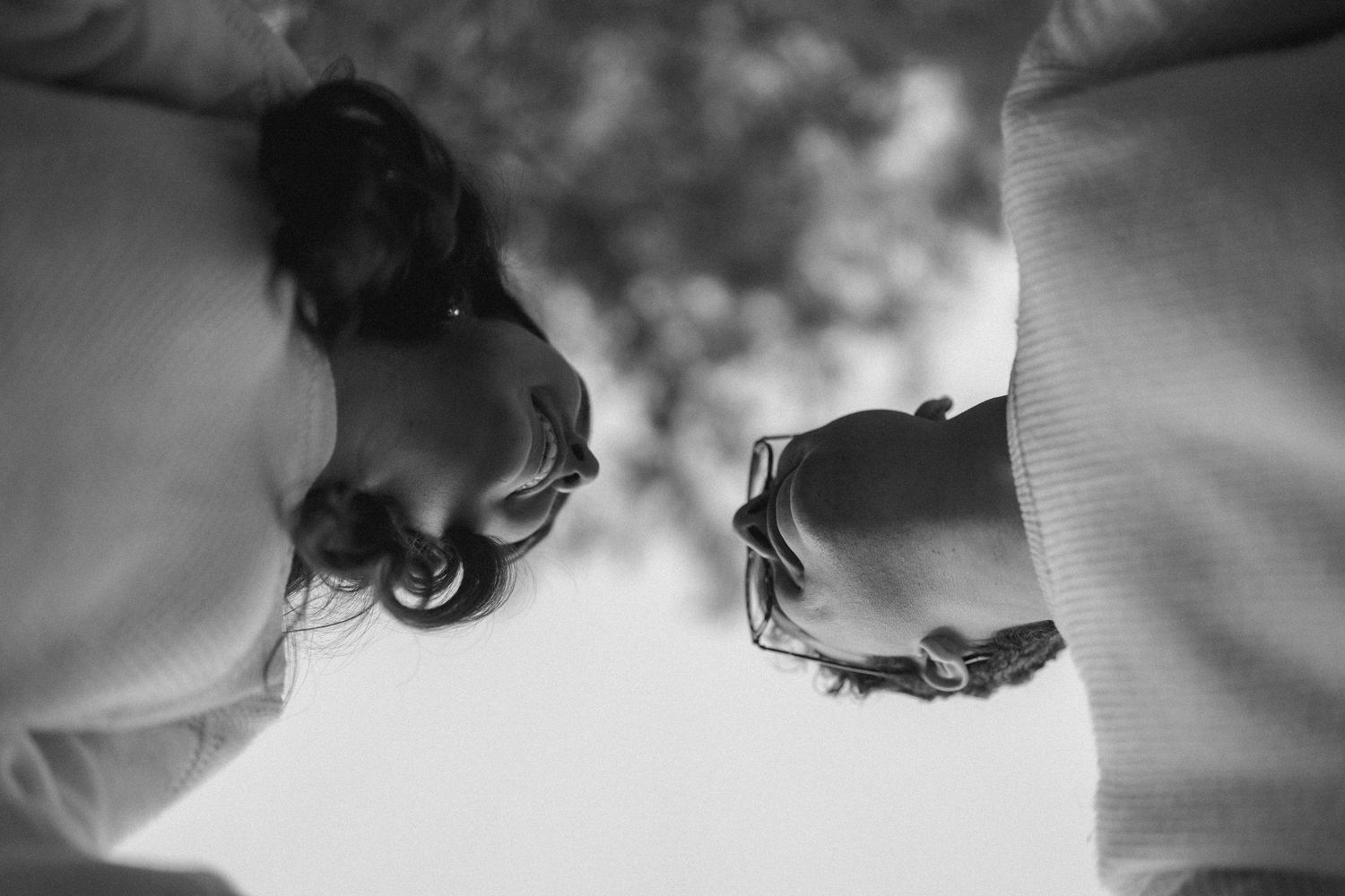 Low angle black and white portrait of couple facing each other against cloudy sky.