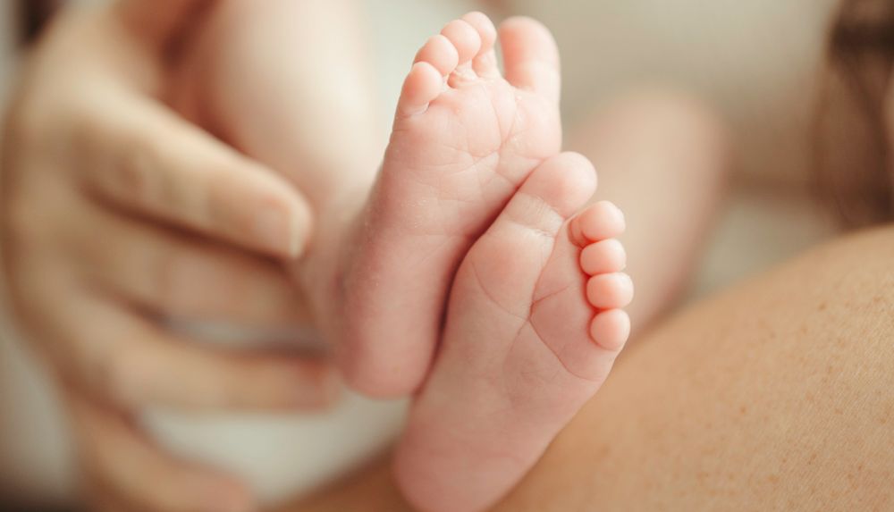 Close-up of tiny newborn baby feet held gently by parent's hands.