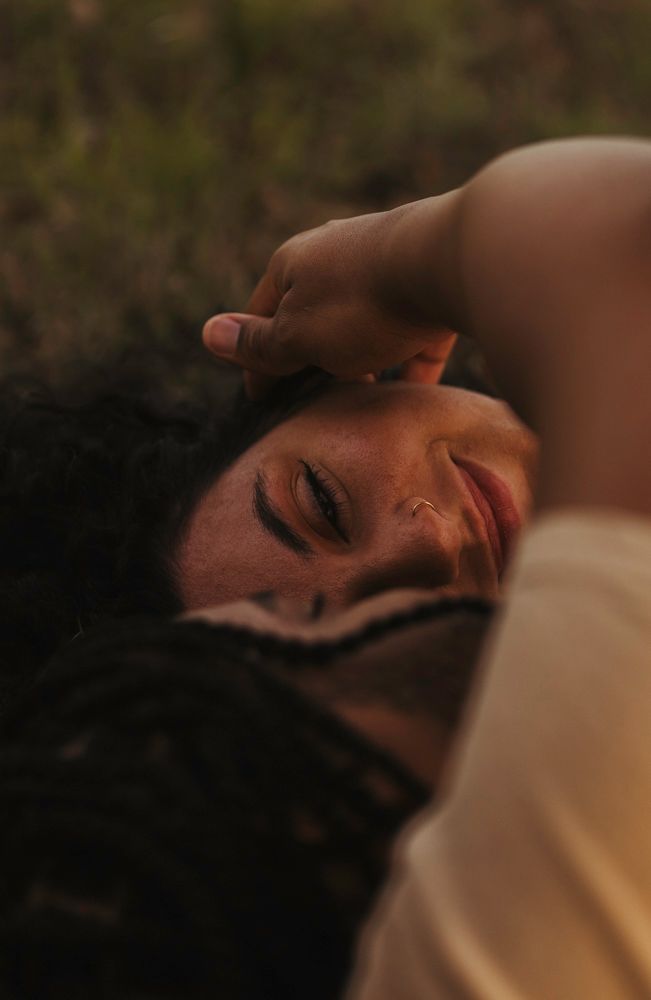Woman with curly hair lying on ground eyes closed in peaceful dreamy outdoor portrait.