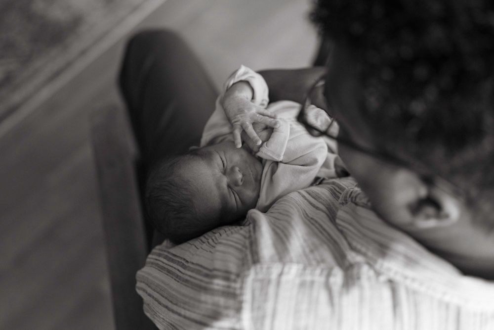 Black and white photo of father tenderly holding sleeping newborn baby against his chest.