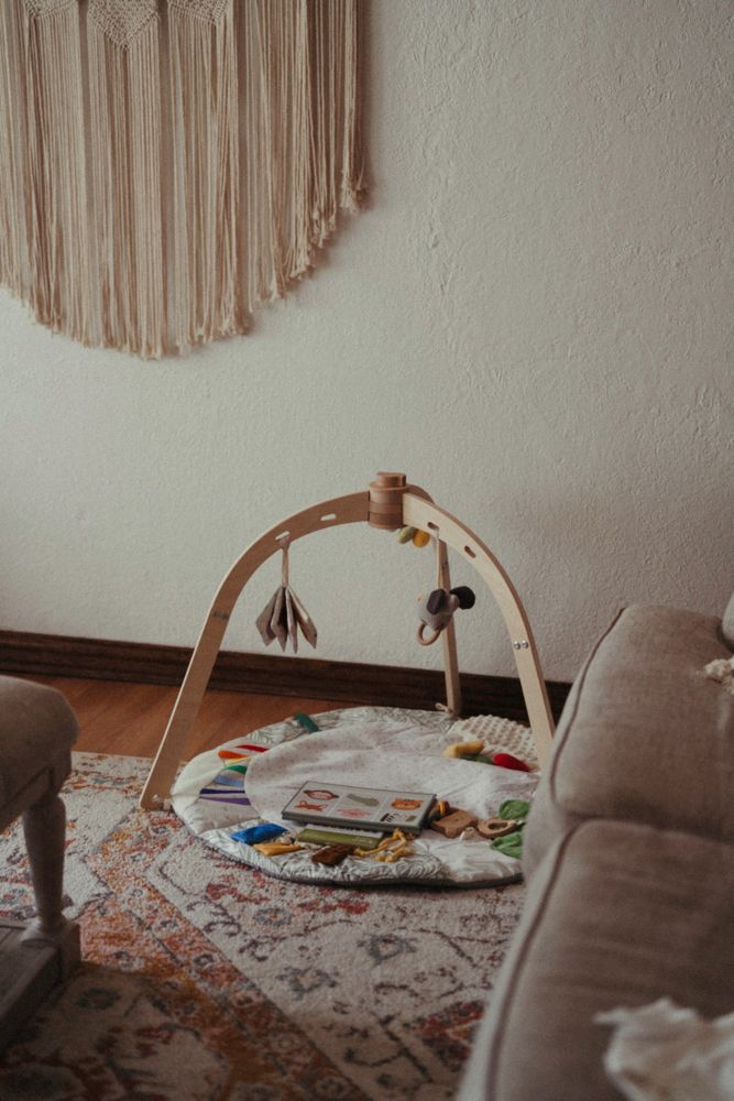 Wooden baby activity gym with hanging toys on a round play mat in a cozy boho nursery.