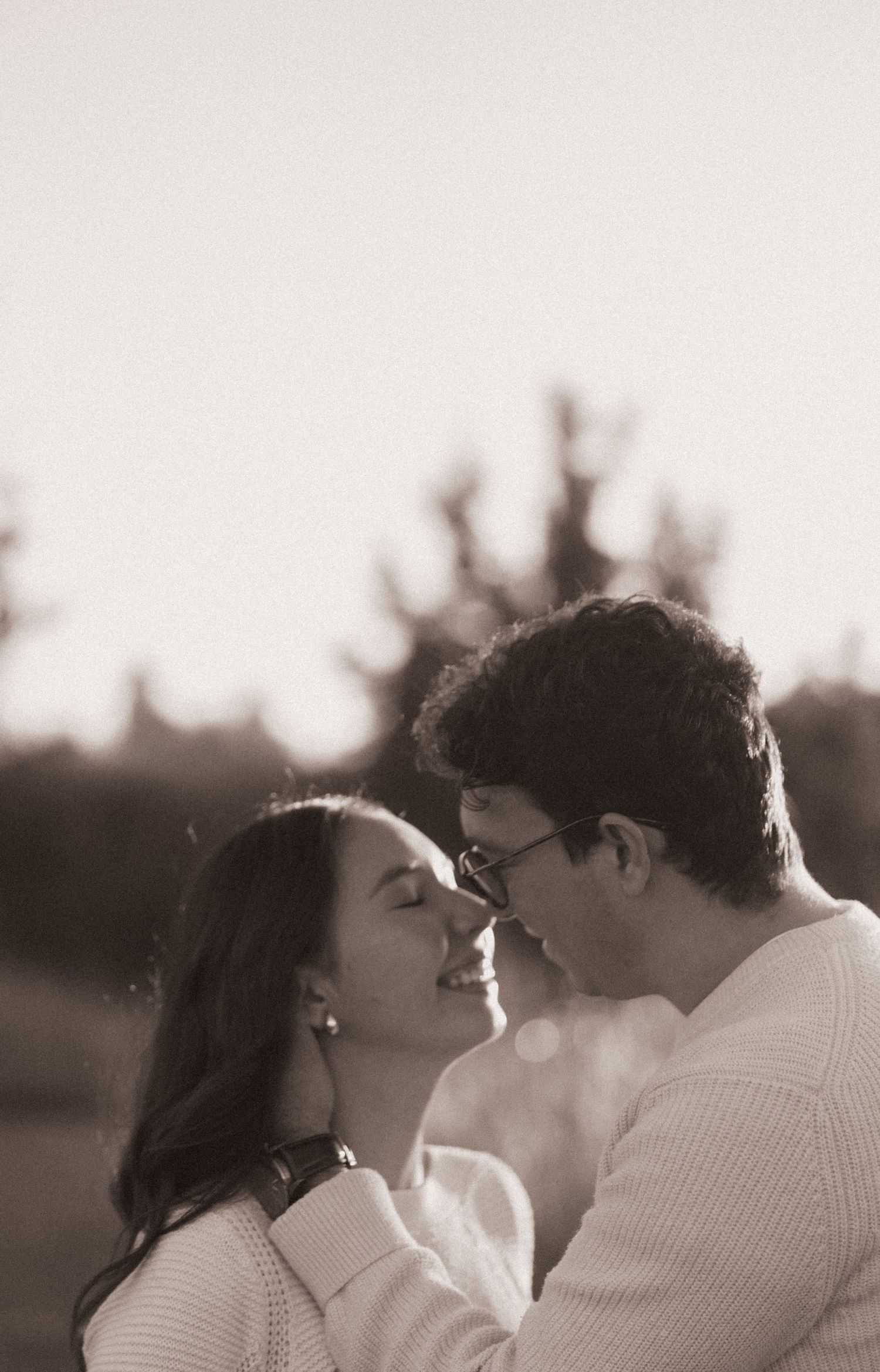 Couple leaning in for a kiss at golden hour in soft black and white portrait.