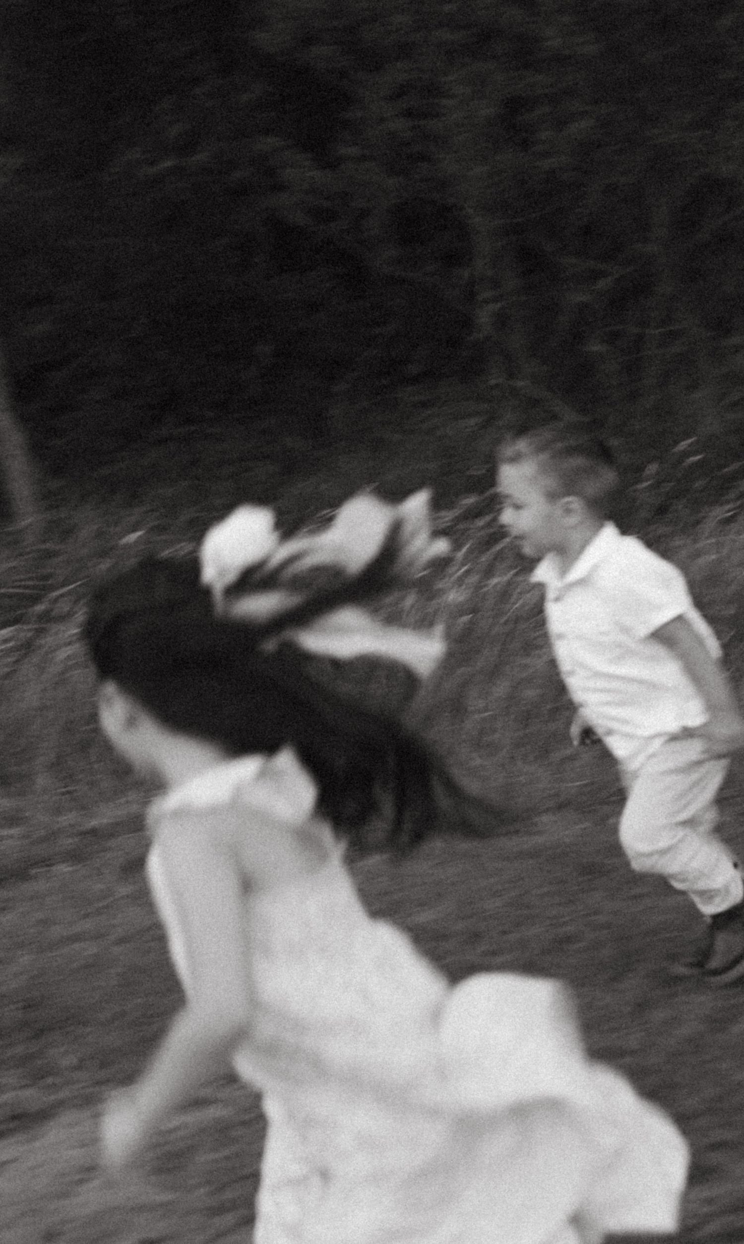 Blurred black and white action shot of children laughing and running outdoors together.