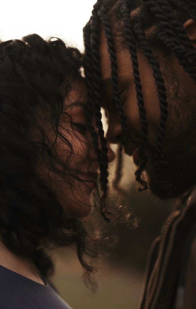 Close-up of a couple with braided and curly hair touching foreheads in an intimate outdoor moment.