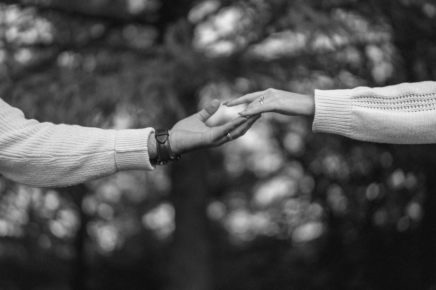 Couple reaching out to hold hands in romantic black and white outdoor portrait.