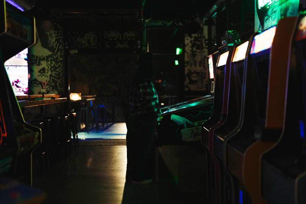 Dimly lit retro arcade bar with glowing neon lights and vintage arcade machines in a dark atmospheric setting.
