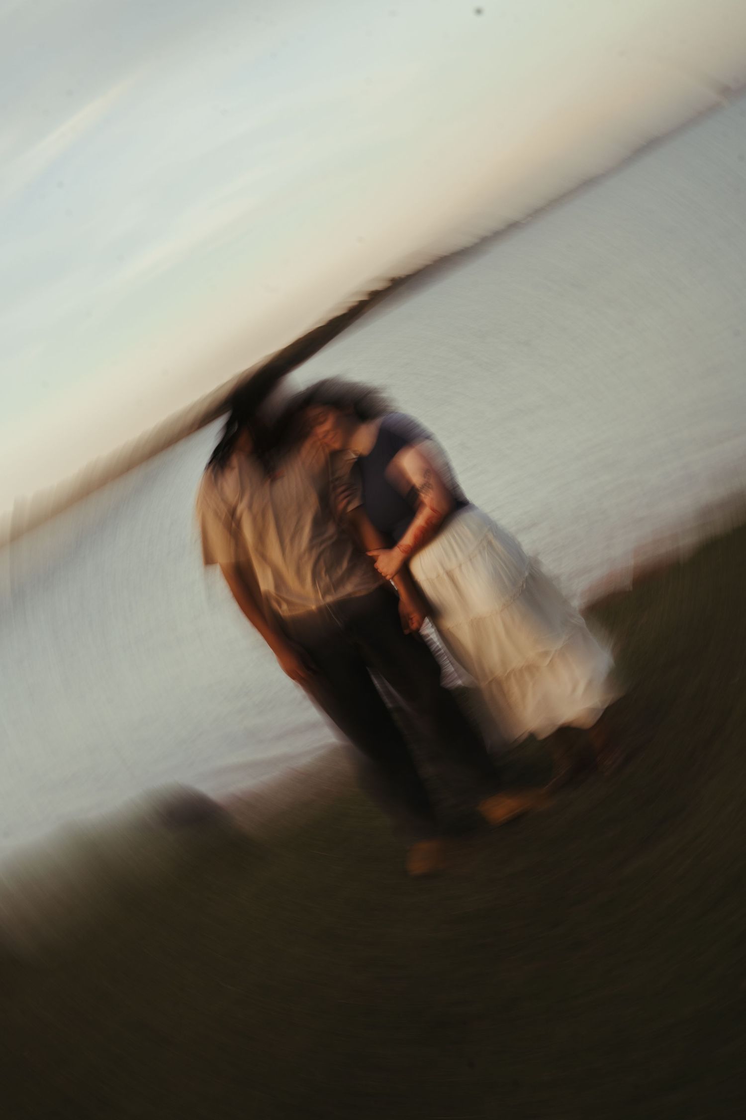 Blurry motion blur photo of a couple embracing near a waterfront at sunset.