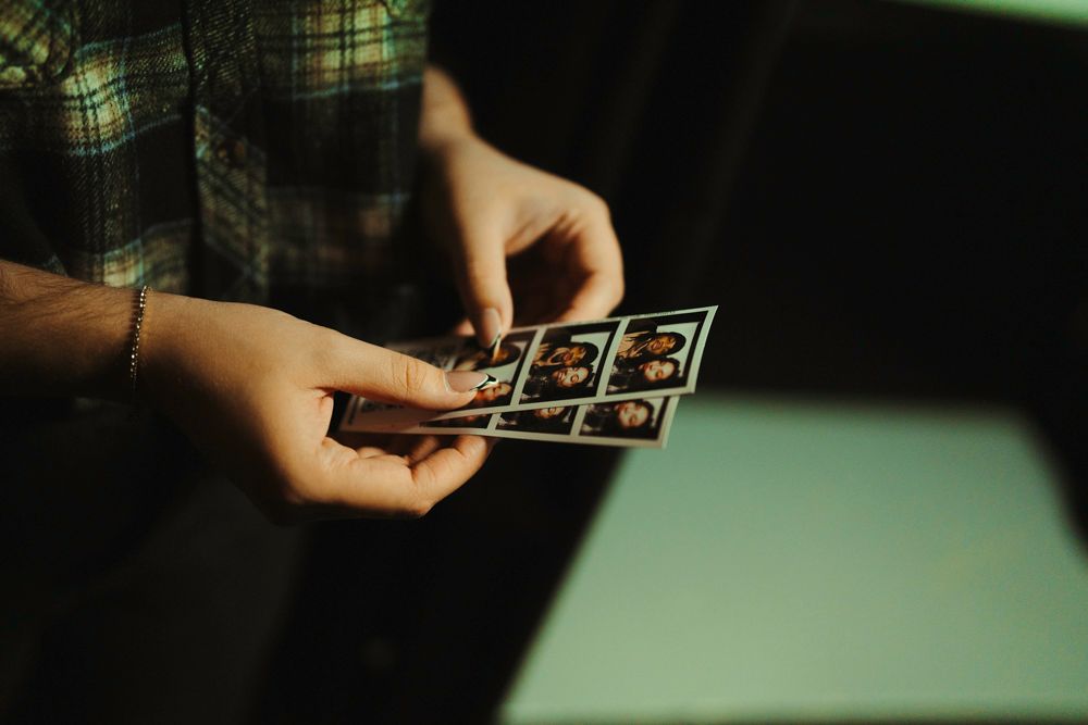 Close-up of hands holding a strip of photo booth pictures in soft green light.