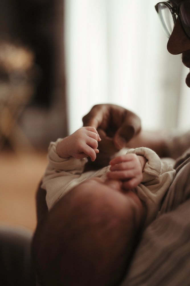 Close-up of newborn baby tiny hands resting on parent's chest in warm ambient light.