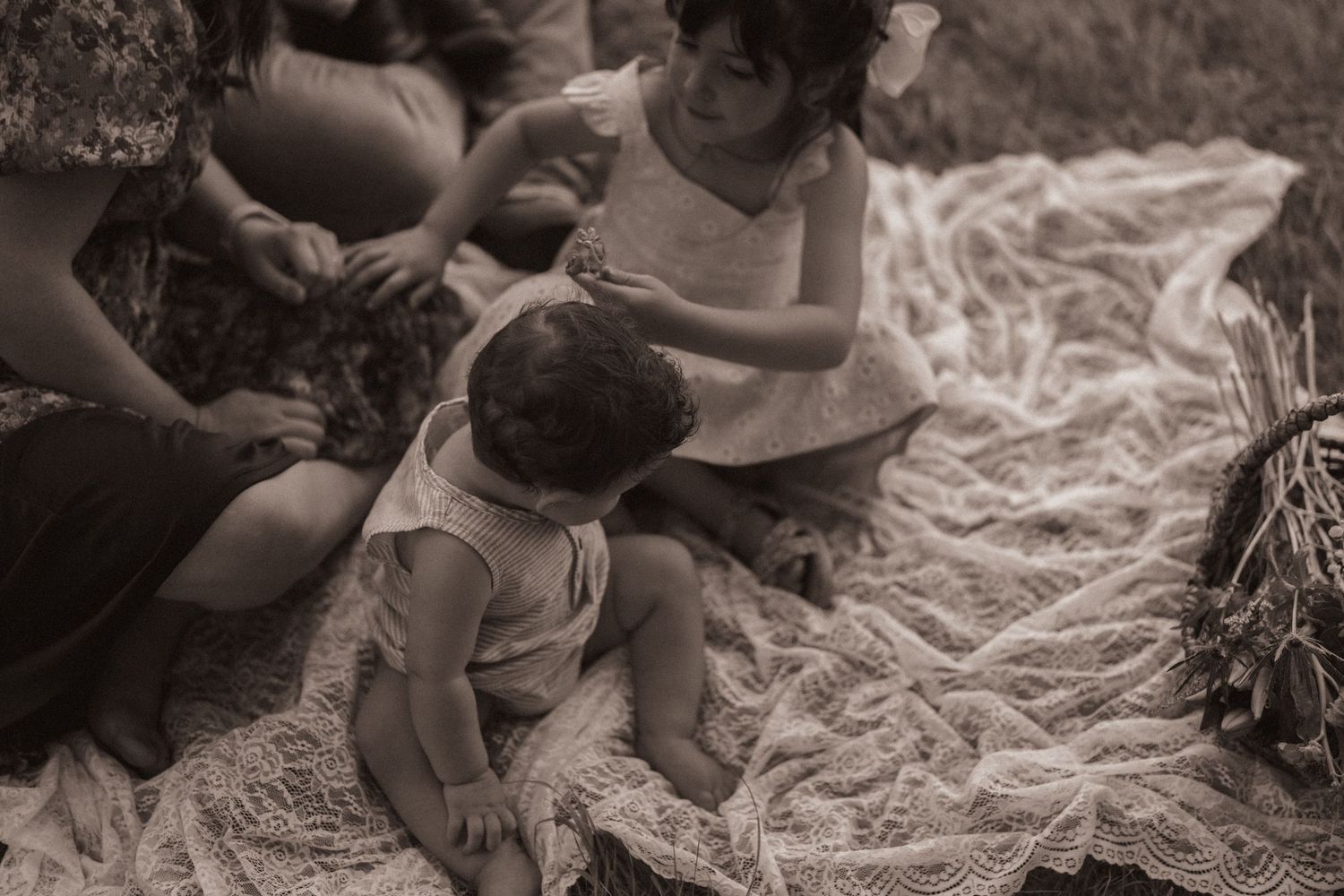 Sepia-toned photo of two young children playing together on a lace blanket outdoors.