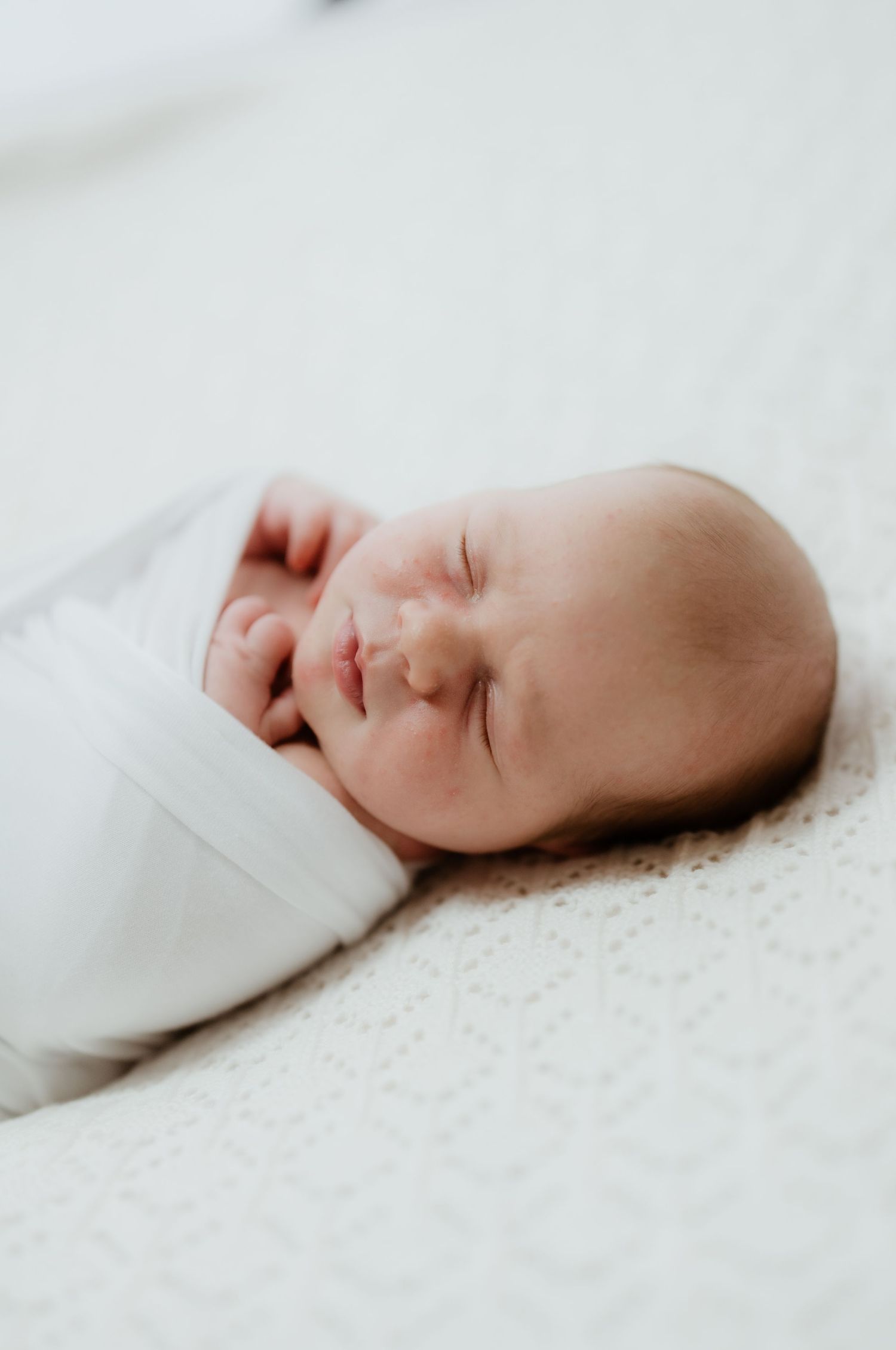 Peaceful newborn baby swaddled in white sleeping on a knit blanket.