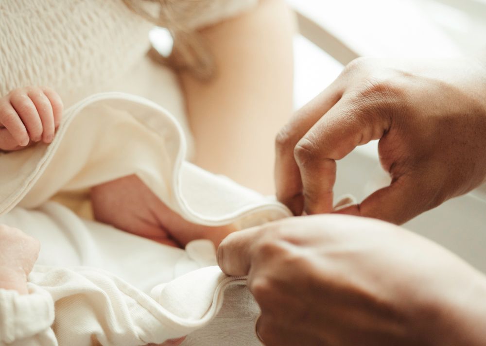 Father carefully fastening buttons on newborn baby's white onesie with gentle hands.