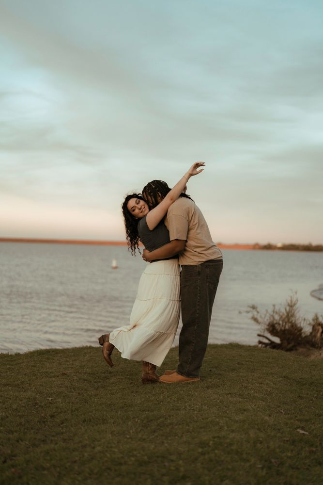 Couple dancing and embracing on grassy lakeside at sunset in joyful romantic portrait.