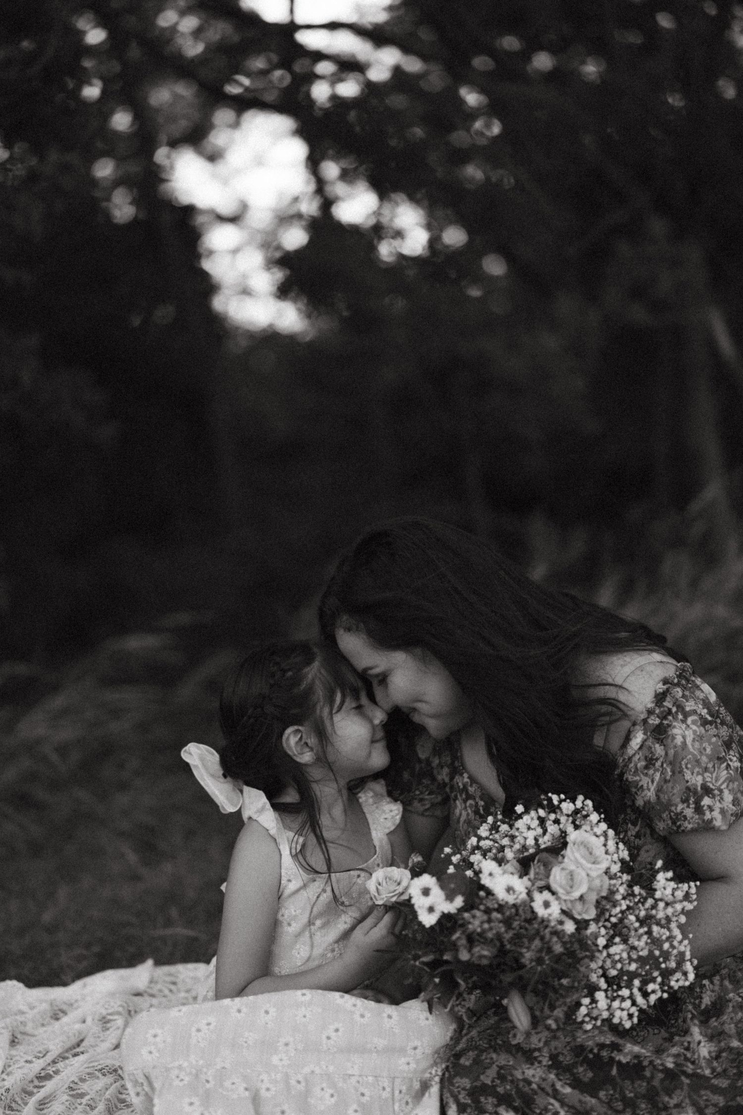 Black and white photo of a mother and daughter touching foreheads tenderly while holding wildflowers.