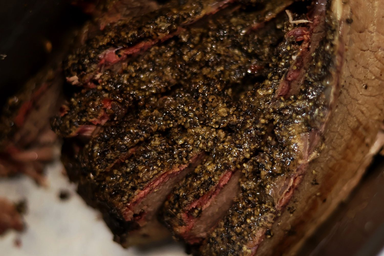 Close-up of herb and pepper crusted smoked beef brisket sliced to reveal juicy, tender meat inside.
