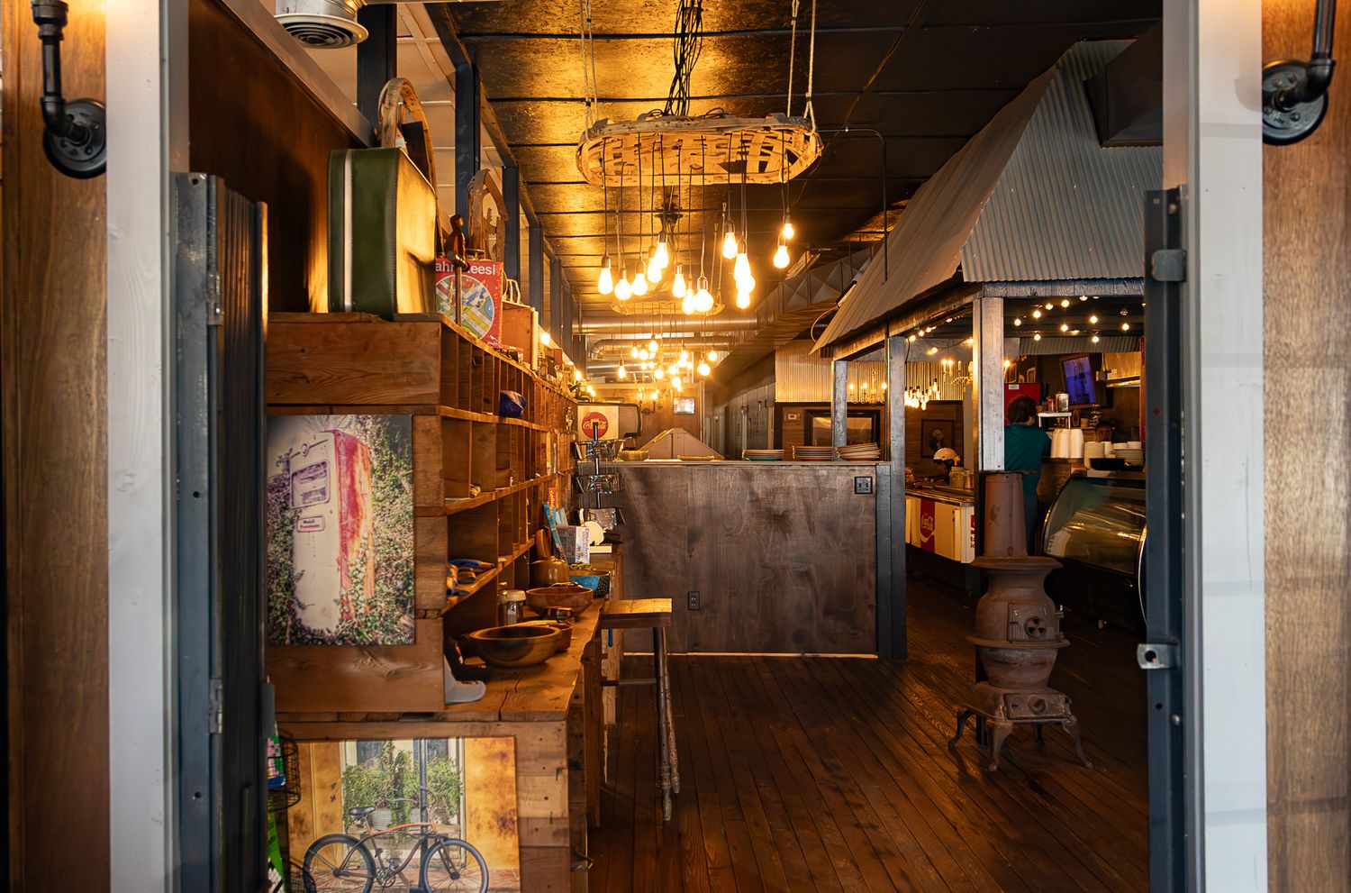Rustic shop interior with warm Edison bulb lighting, wooden shelves, and vintage decor along a narrow corridor.