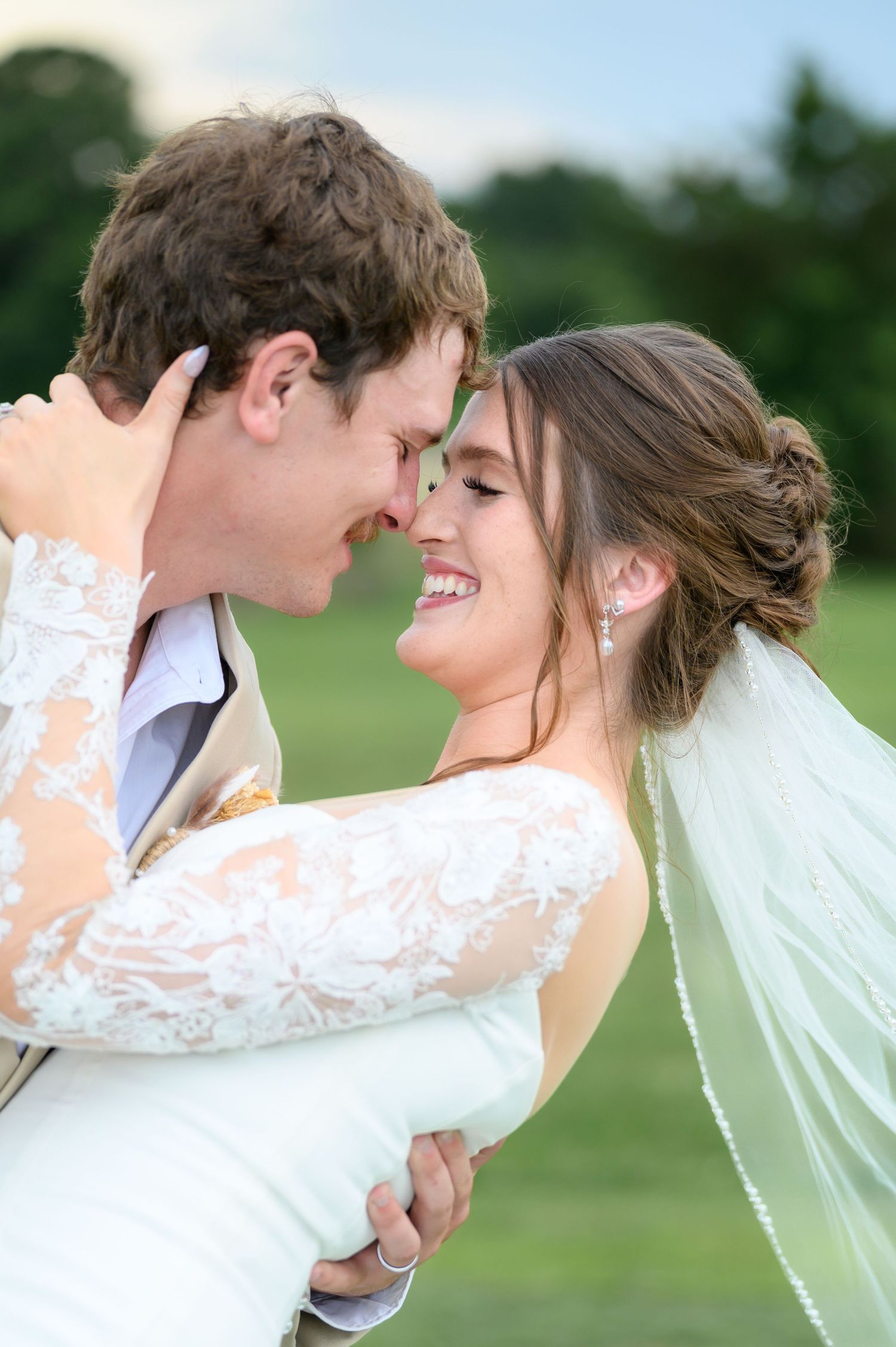 Laughing bride and groom touch foreheads in a joyful embrace on their wedding day outdoors.