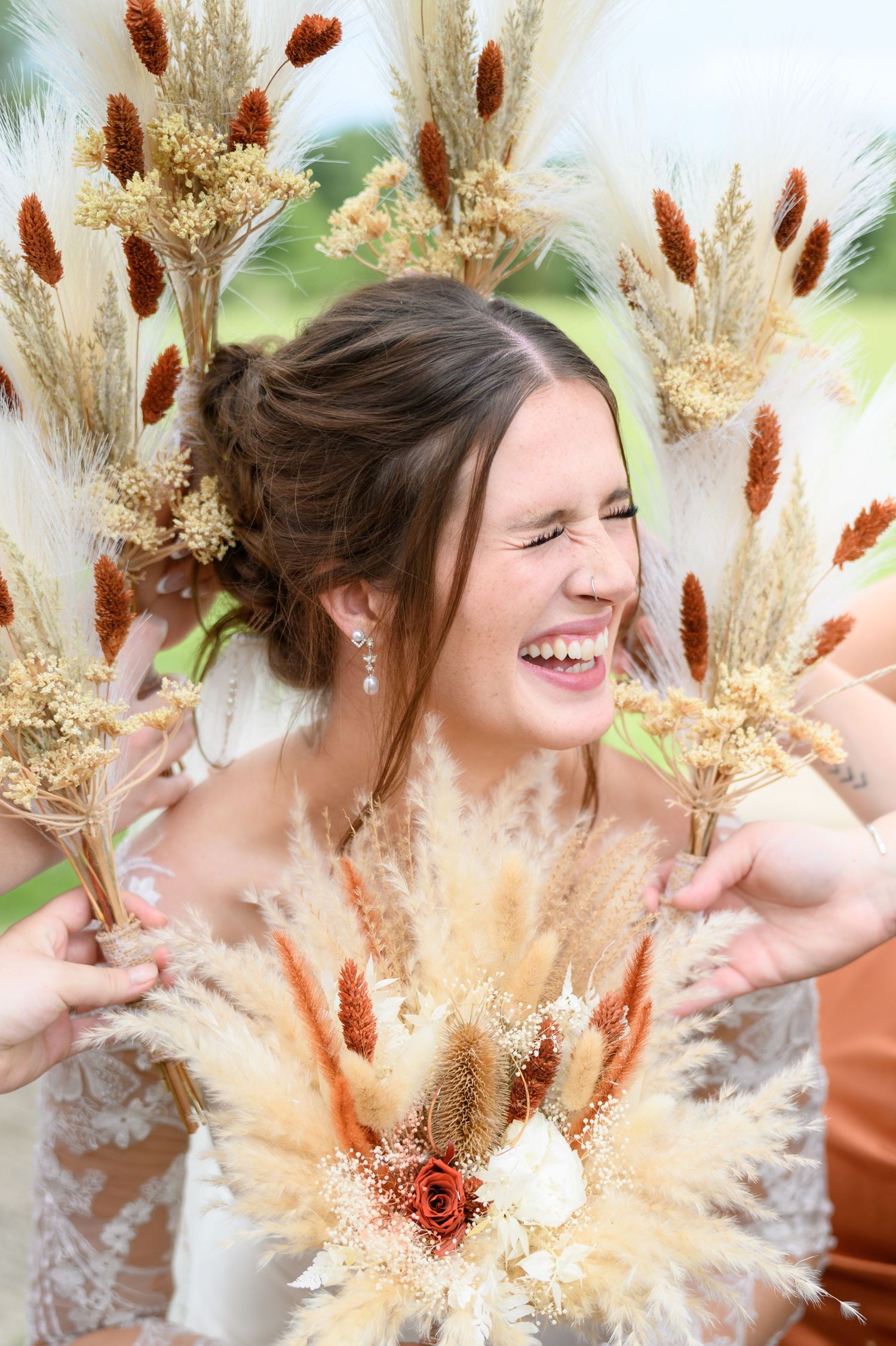 Laughing bride surrounded by dried pampas grass and wheat bouquets on her wedding day.