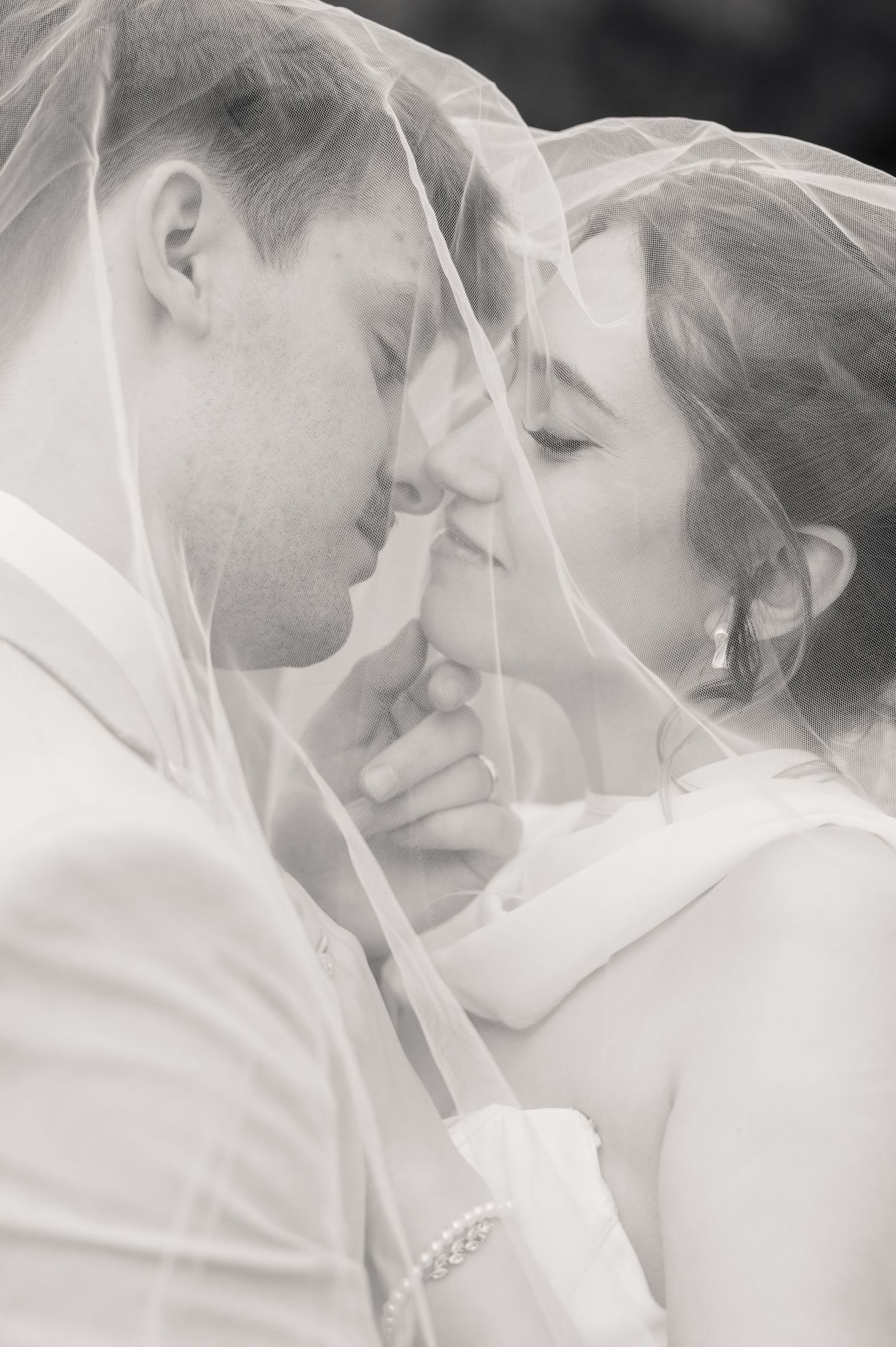 Black and white photo of a bride and groom sharing an intimate moment under a wedding veil.