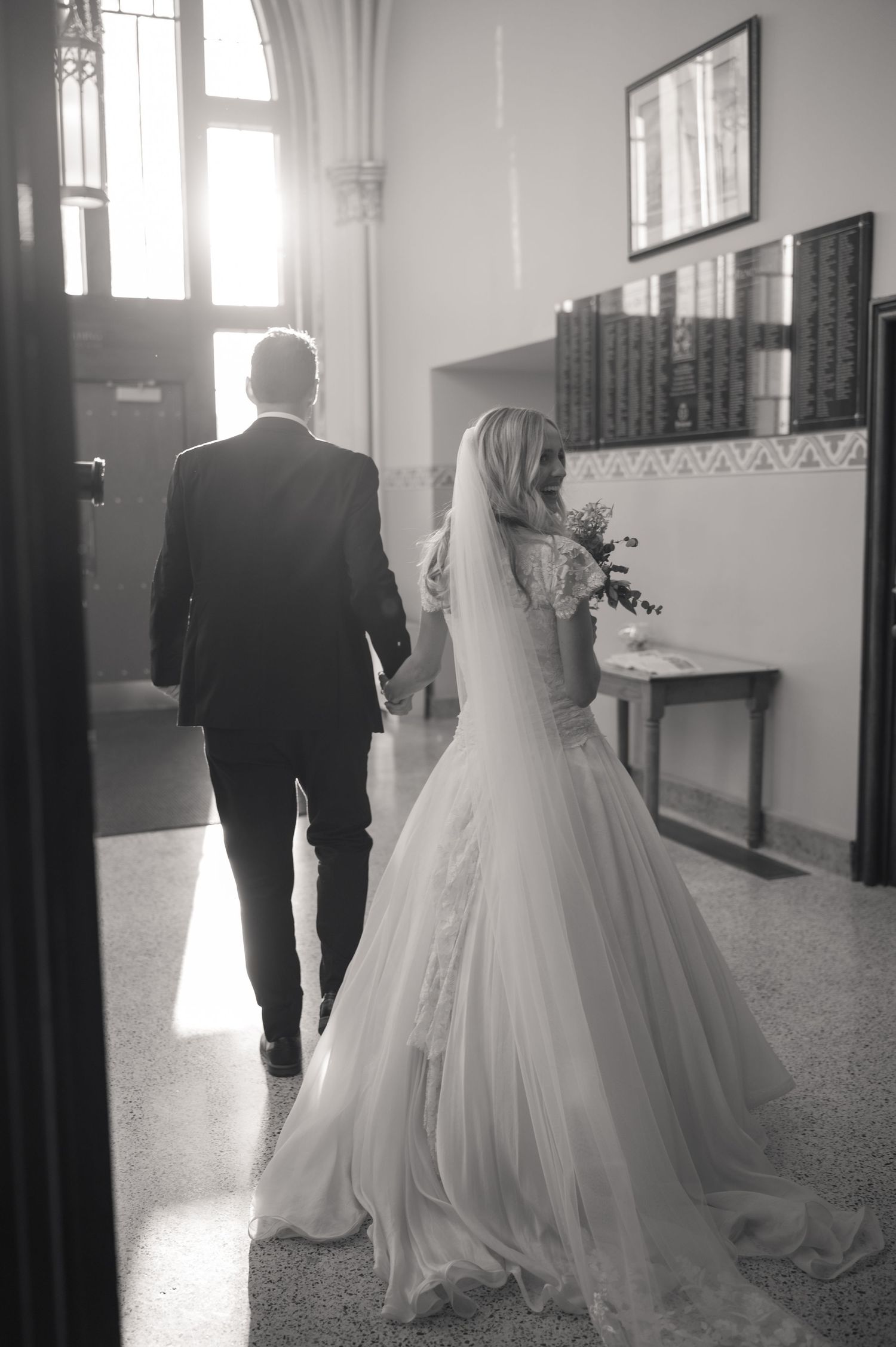 Black and white photo of bride and groom walking out of church entrance after ceremony.