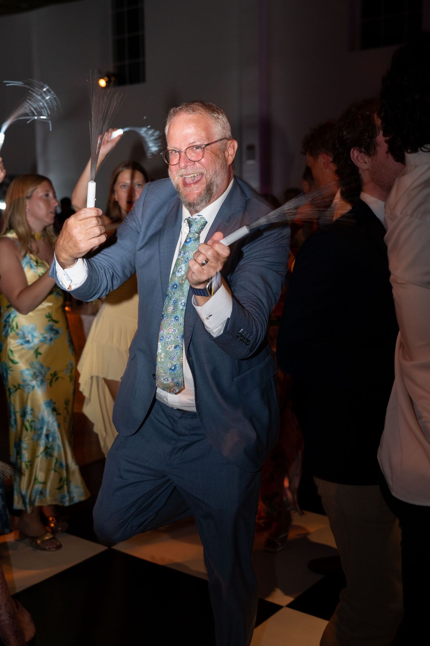 Energetic wedding guest dances with glowsticks on black and white dance floor.