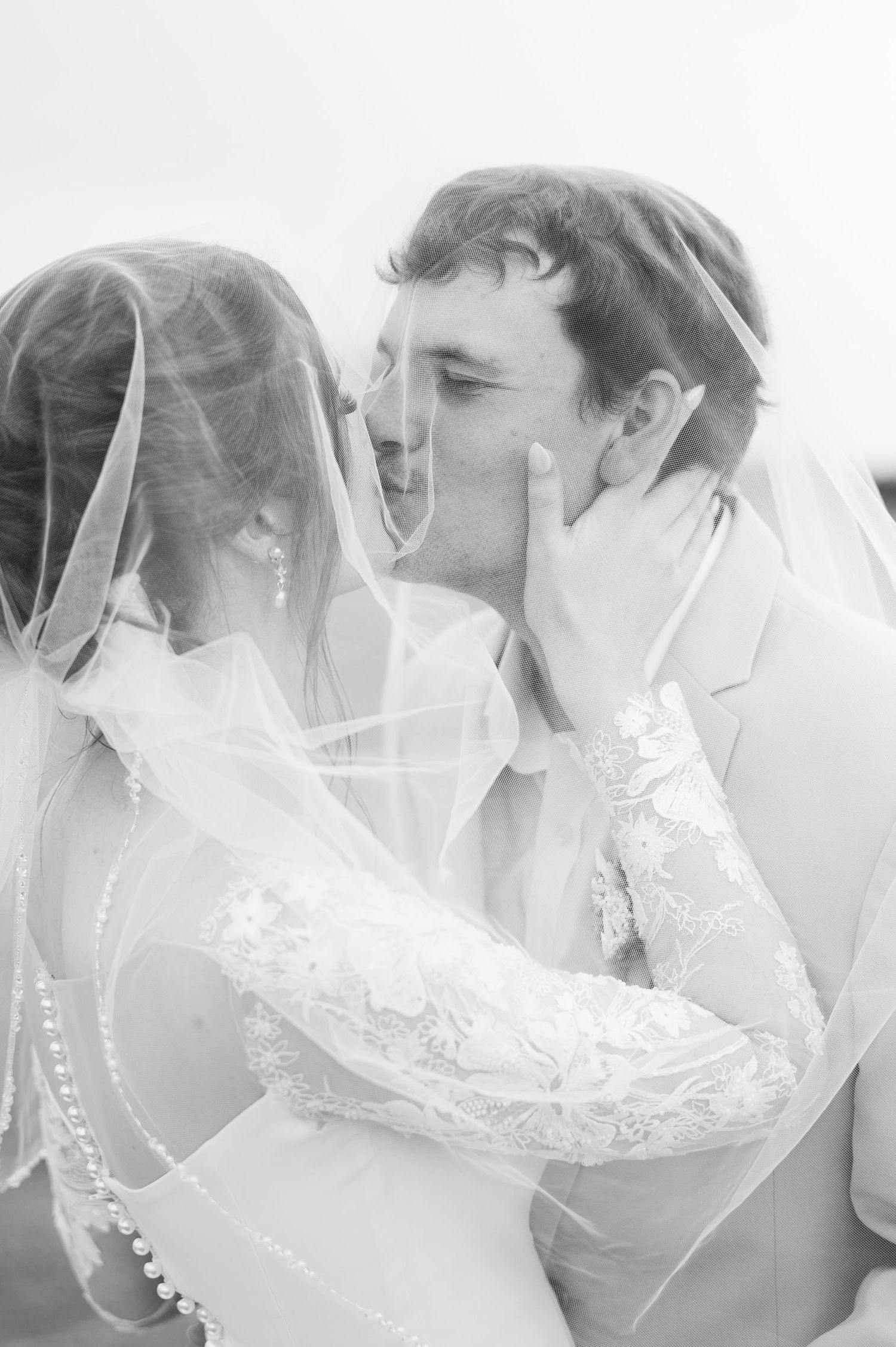 Black and white photo of bride and groom about to kiss under flowing wedding veil.