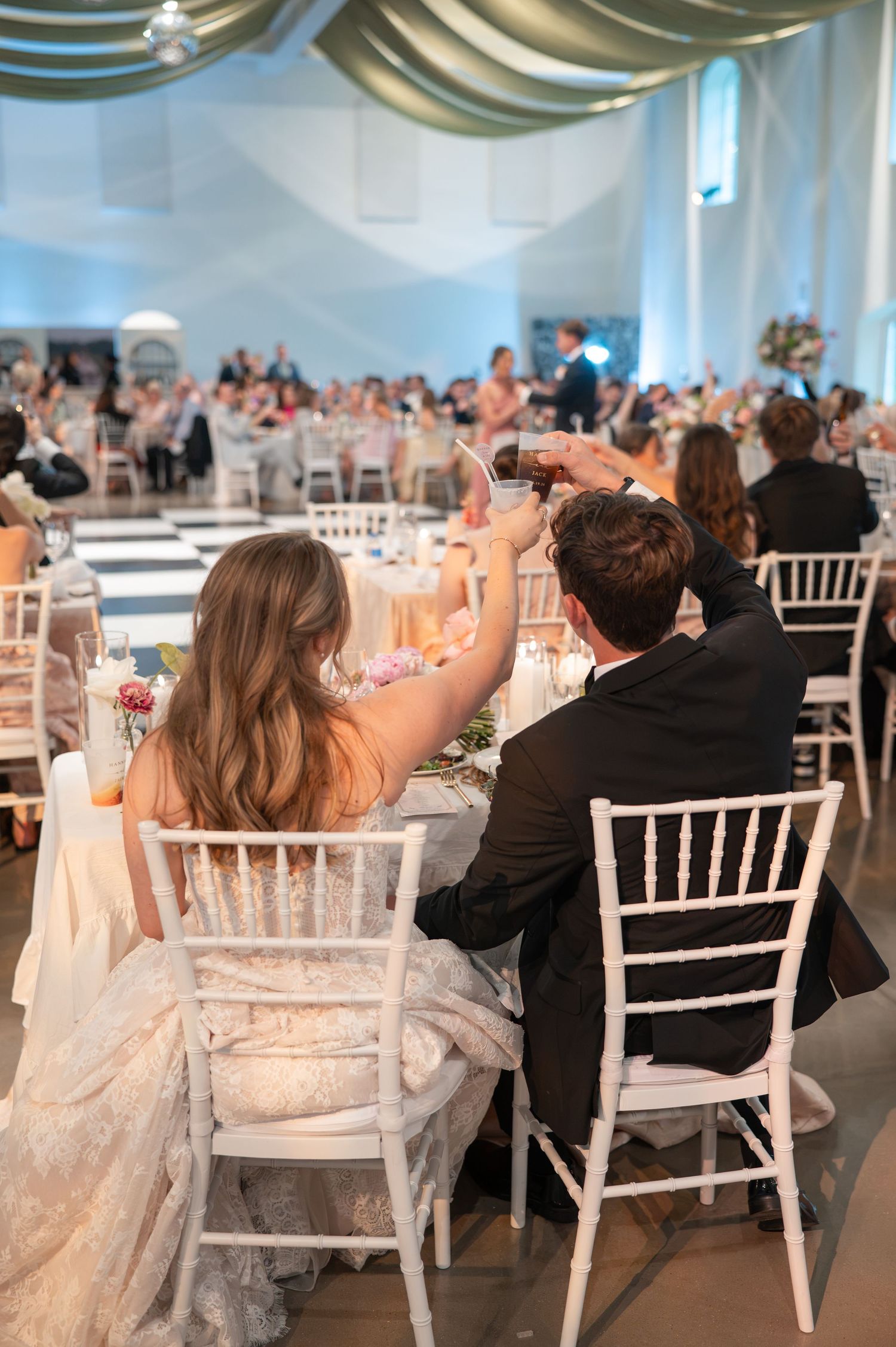 Bride and groom raise glasses for toast at elegant wedding reception.