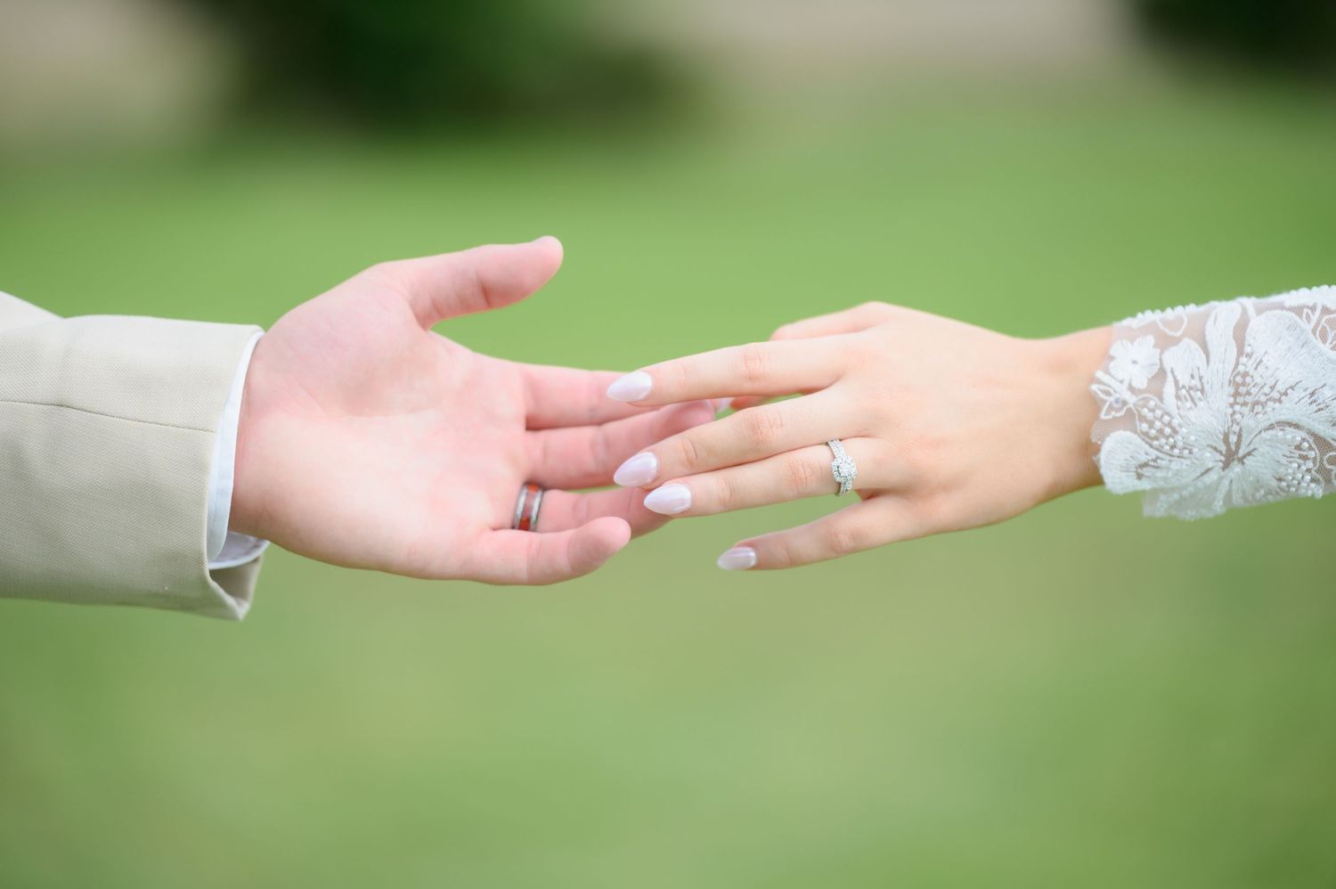 Close-up of bride and groom reaching hands toward each other, bride wearing diamond wedding ring.
