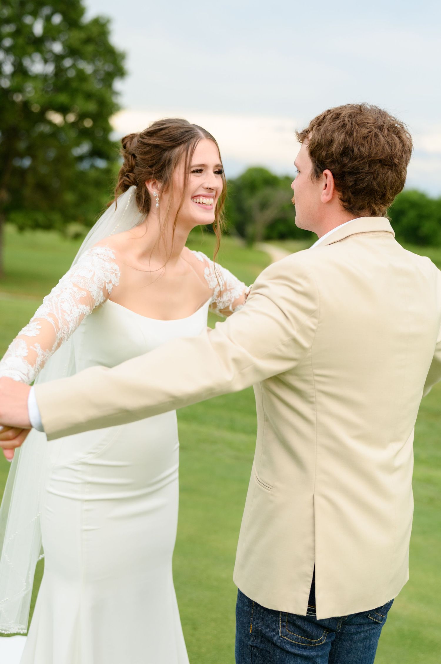 Bride smiling warmly at groom while dancing together on green lawn at outdoor wedding celebration.