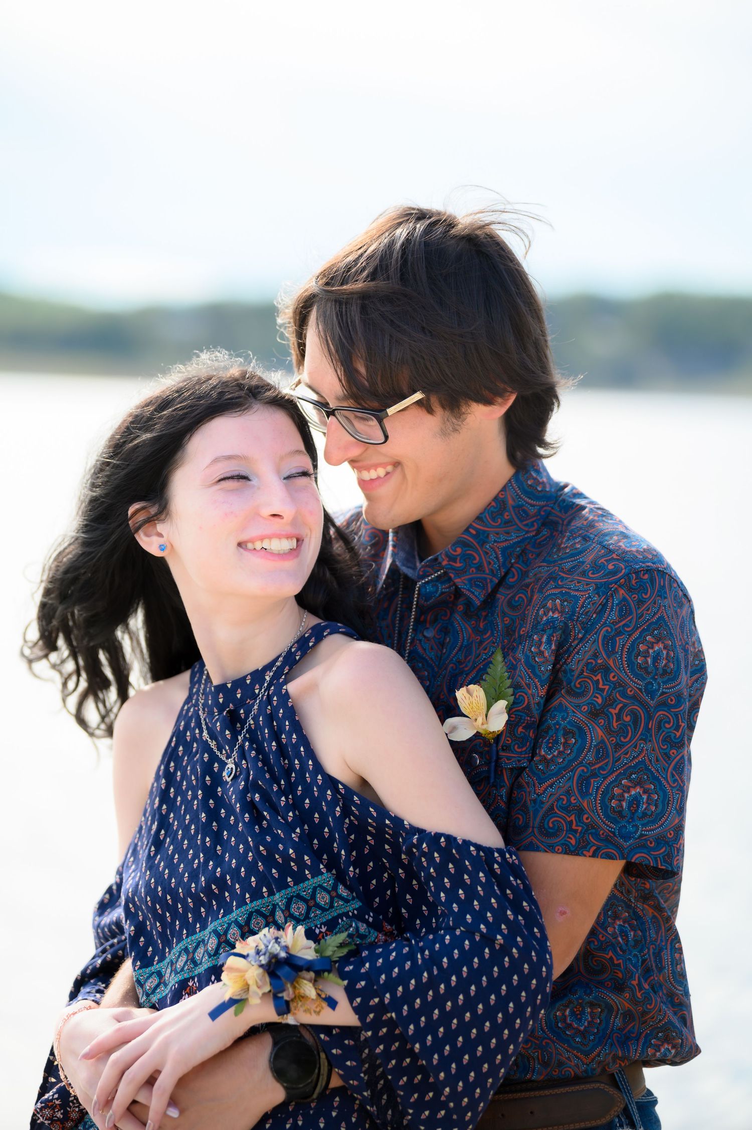 Young couple embracing and smiling together near a sparkling waterfront.