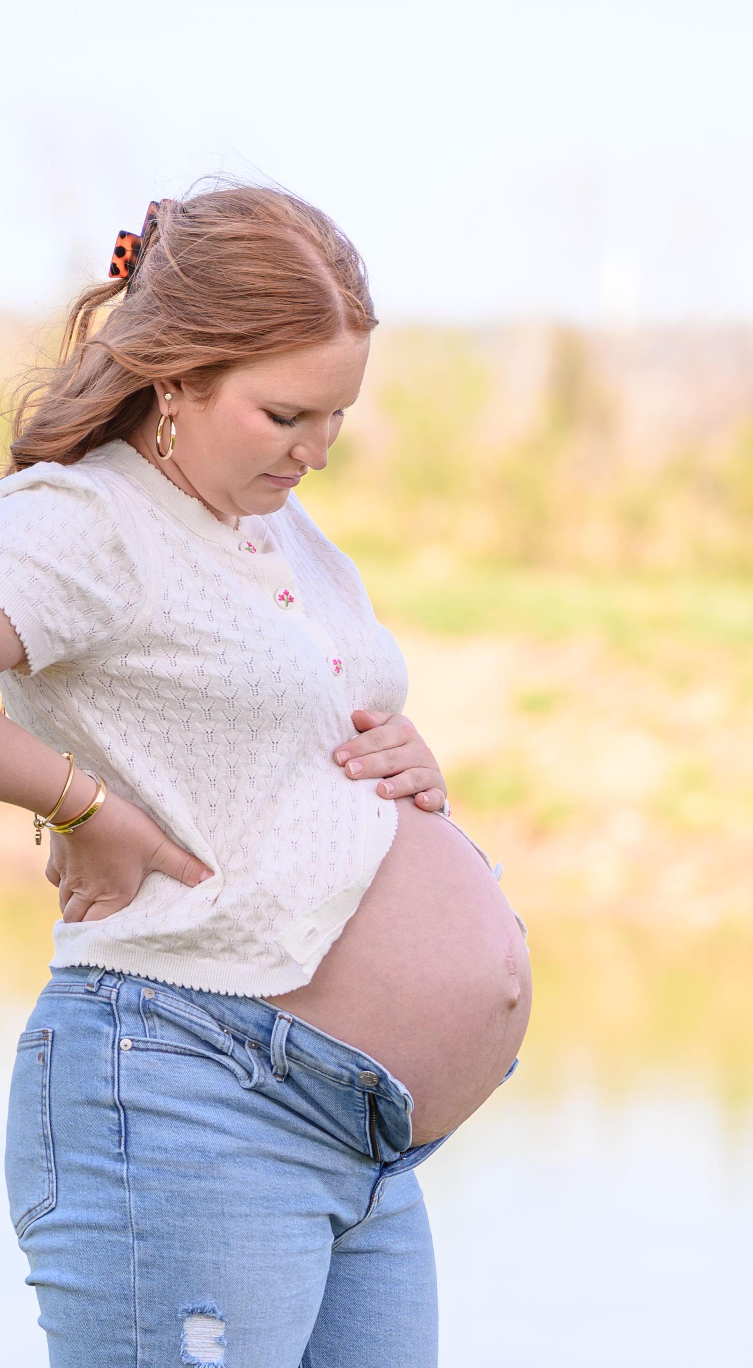 Pregnant woman cradling her baby bump outdoors in natural light.