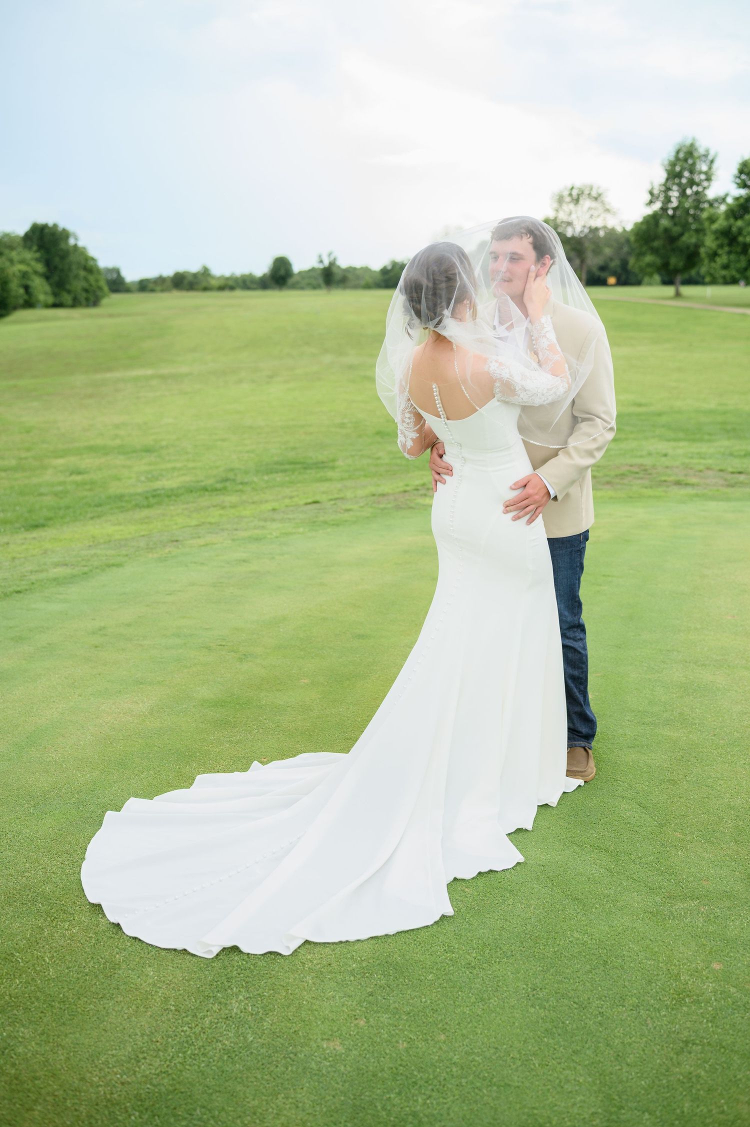 Bride and groom share a kiss under her veil on a lush green golf course at sunset.