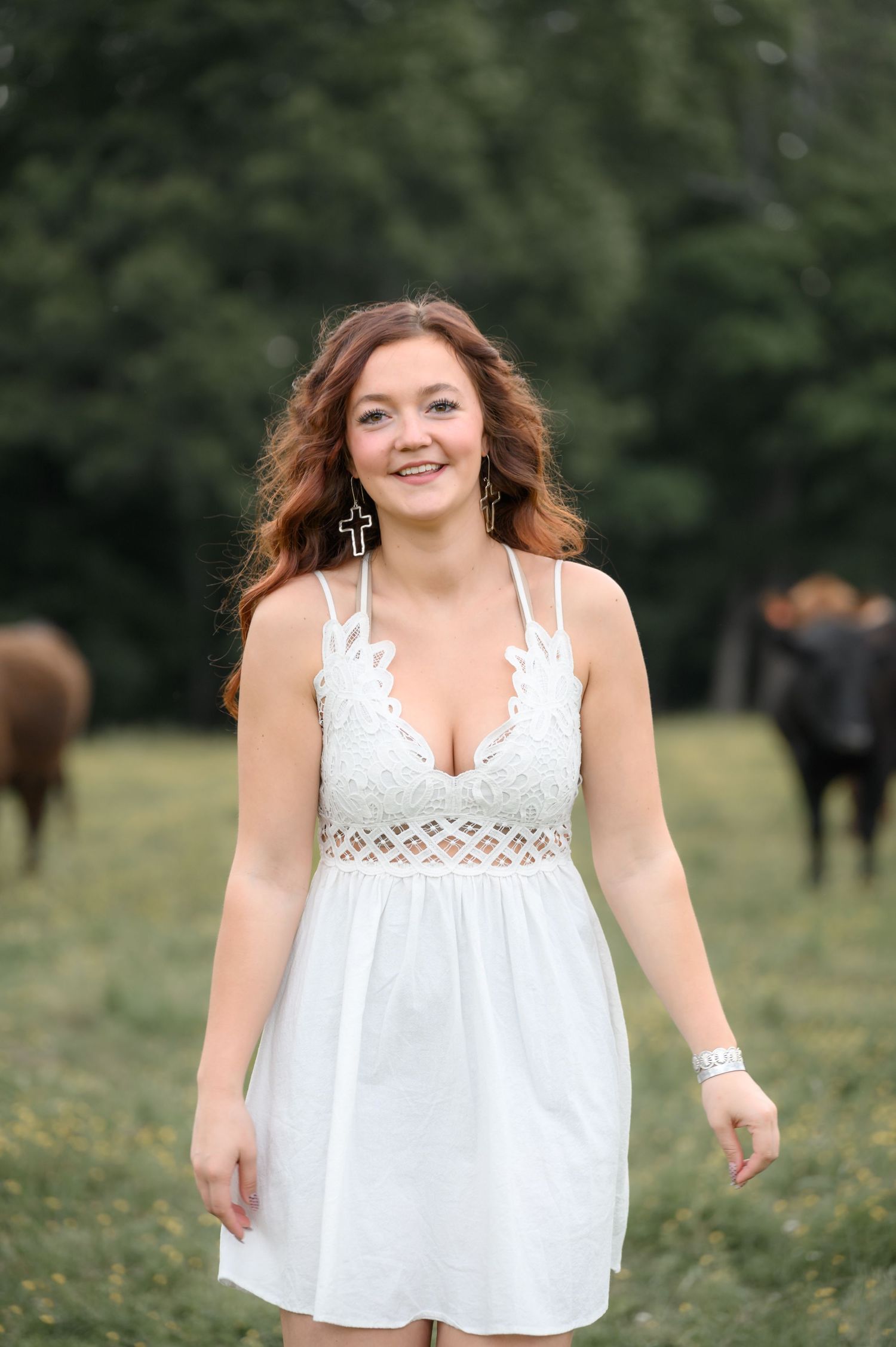 Smiling young woman in a white dress standing in a pasture with cattle.