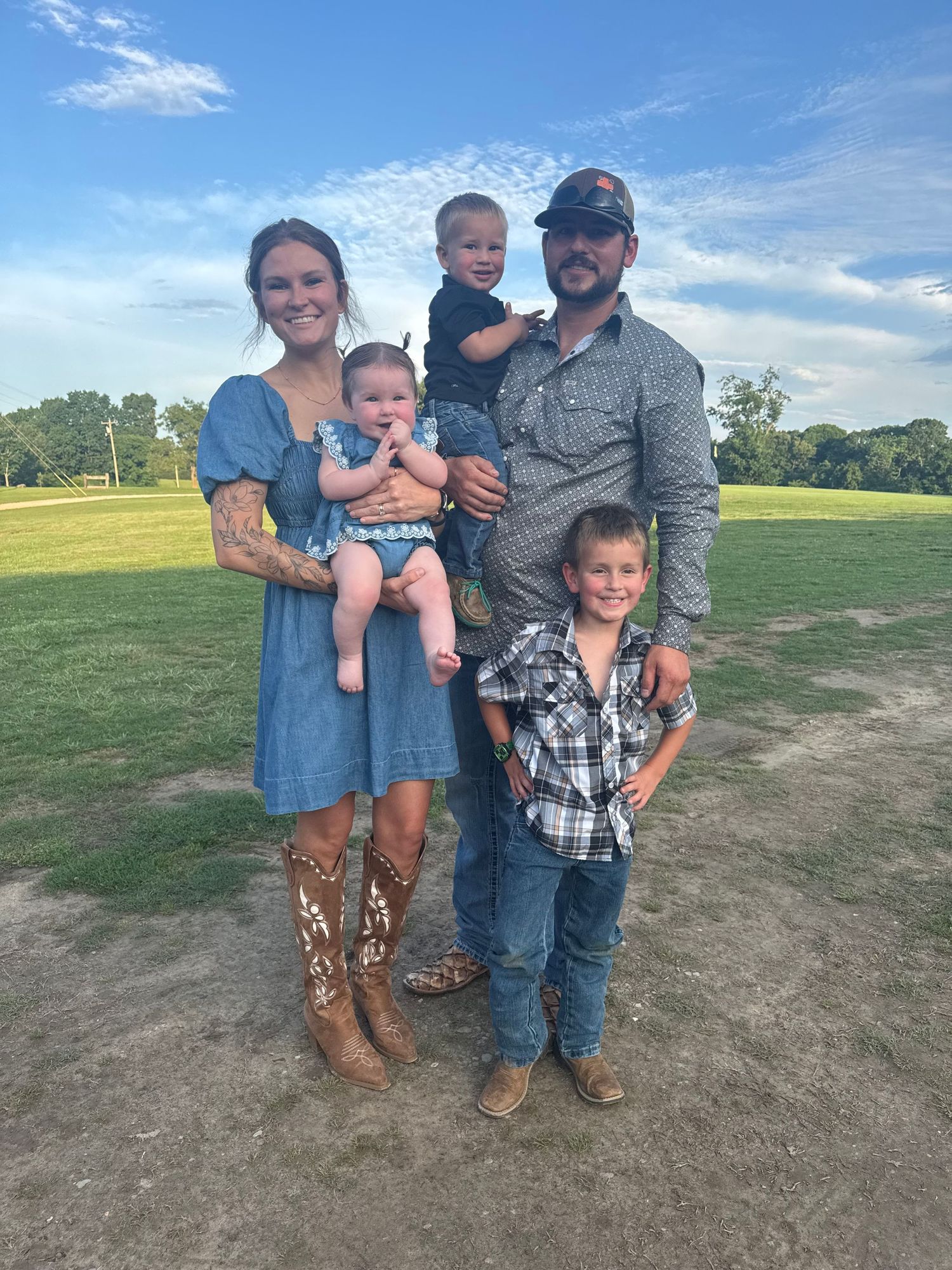 Family of five posing outdoors on a green field, parents holding two toddlers with older child standing in front.