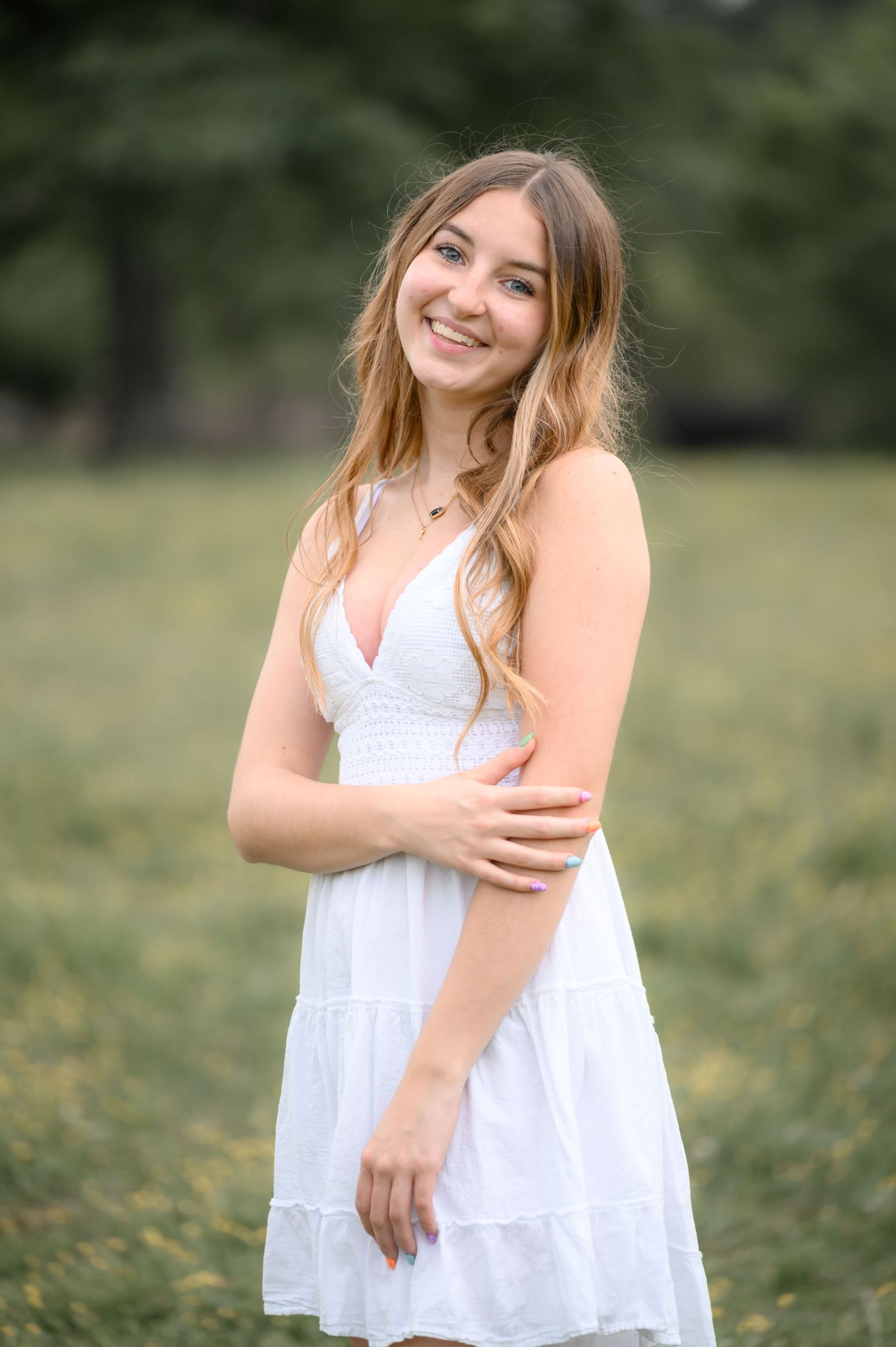 Smiling young woman in a white dress posing in a green field.