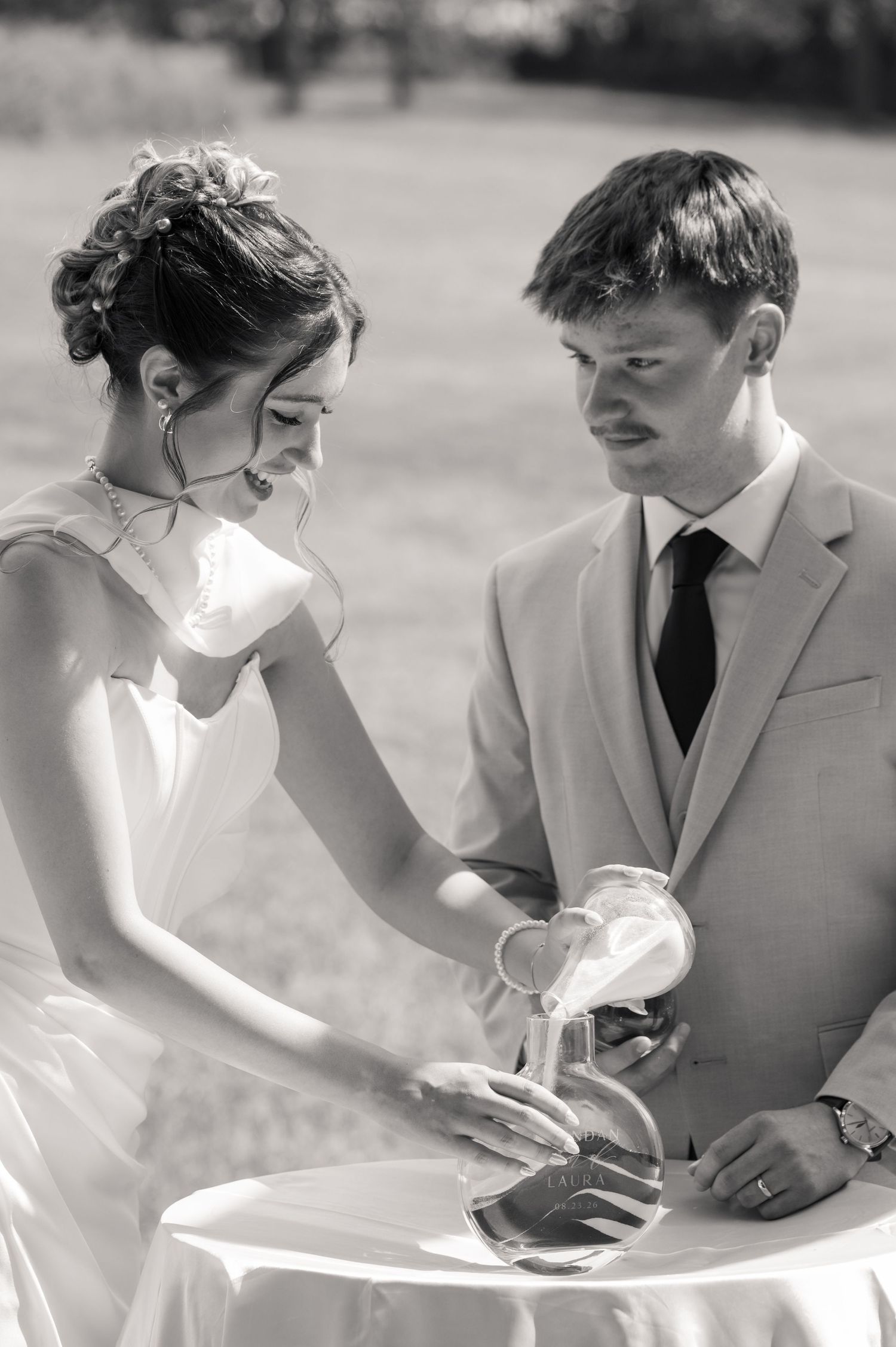 Black and white photo of bride and groom performing a sand unity ceremony at their outdoor wedding.