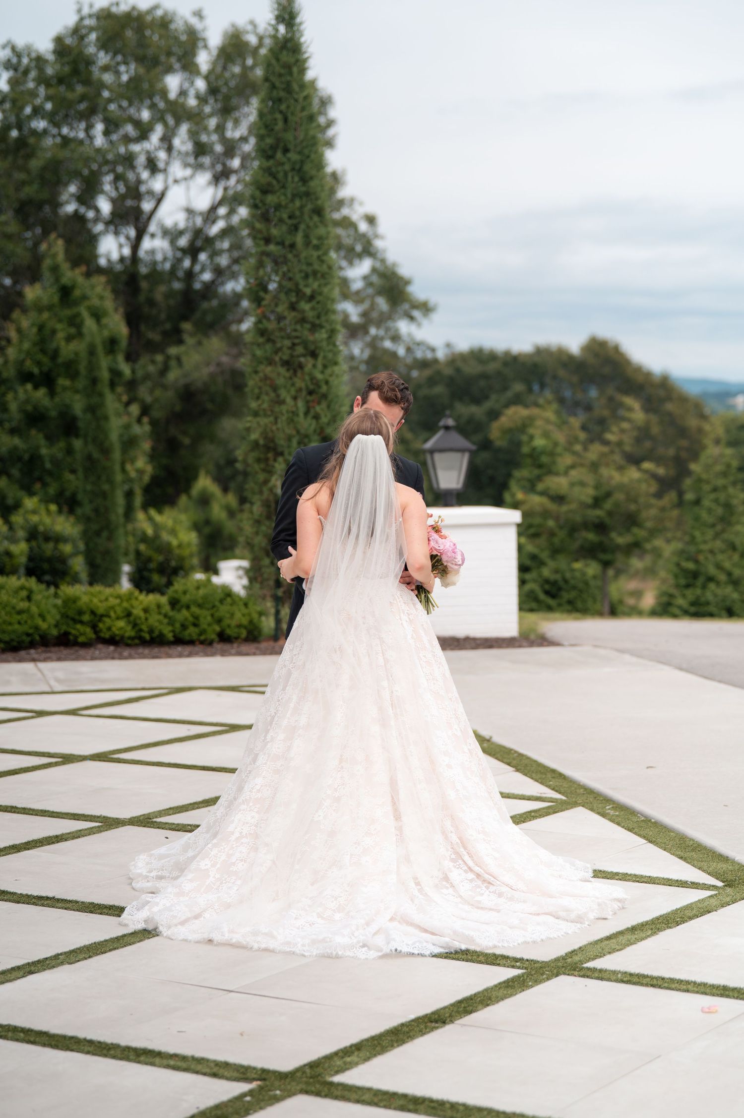 Bride and groom walk away hand in hand, showcasing cathedral lace veil and gown train outdoors.